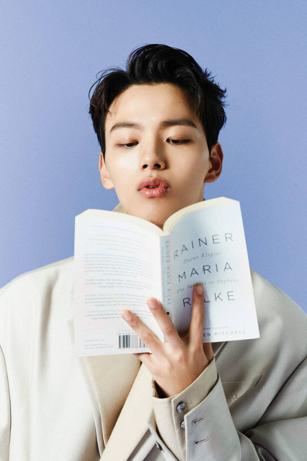 Yeo Jin Goo 與書本 壁紙 — 一位身穿米色西裝的年輕男子在柔和的藍色工作室背景下閱讀一本名為 Rainer Maria Rilke 的書。