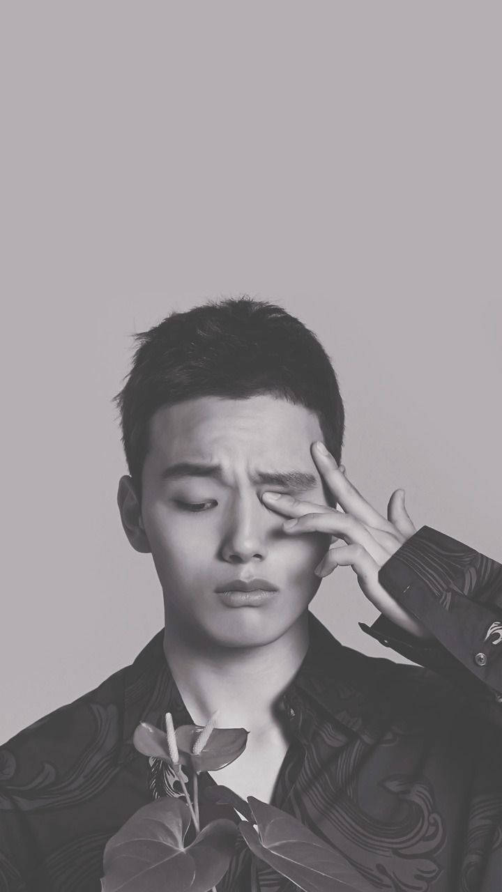 Yeo Jin Goo 與植物 壁紙 — 一個年輕男子用手遮住眼睛，拿著植物，背景單調的黑白肖像。