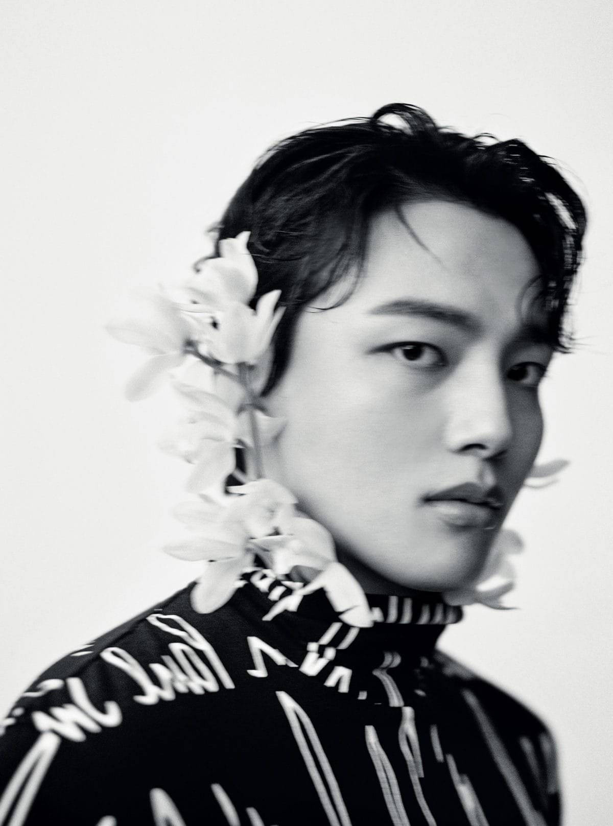 Yeo Jin Goo 花卉背景時尚寫真 壁紙 — 一個年輕黑髮男子的黑白肖像，肩上披著花環，背景簡潔。