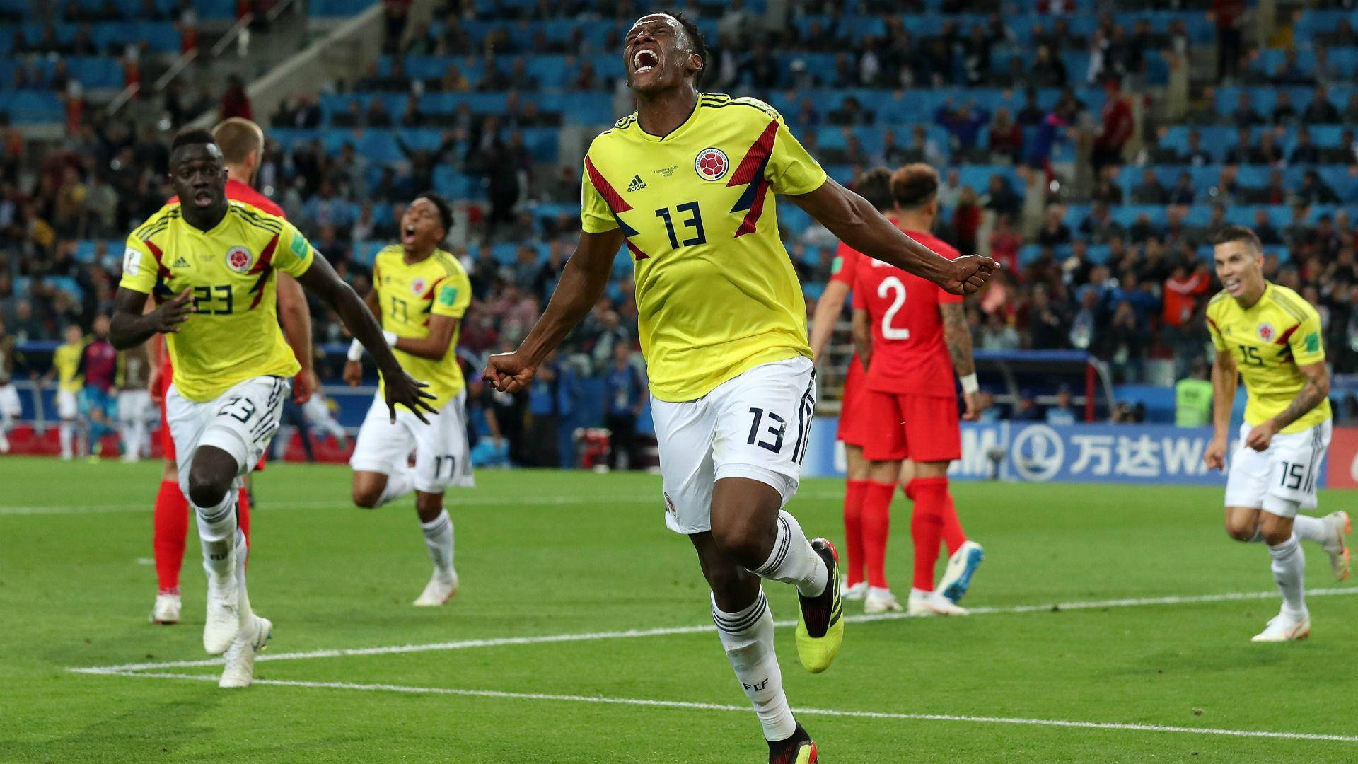 Yerry Mina 場上歡呼奔跑 壁紙 — 哥倫比亞足球員13號在充滿活力的綠色球場上欣喜若狂地跳躍，隊友們在他周圍慶祝。