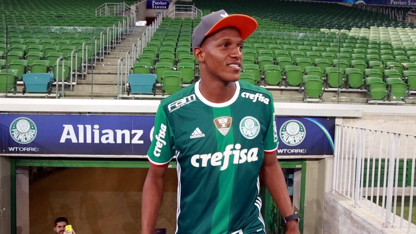 Yerry Mina 空曠球場 壁紙 — 一名身穿綠色和白色球衣的足球員自信地站在一個空蕩蕩的體育場內，身後是綠色座位。