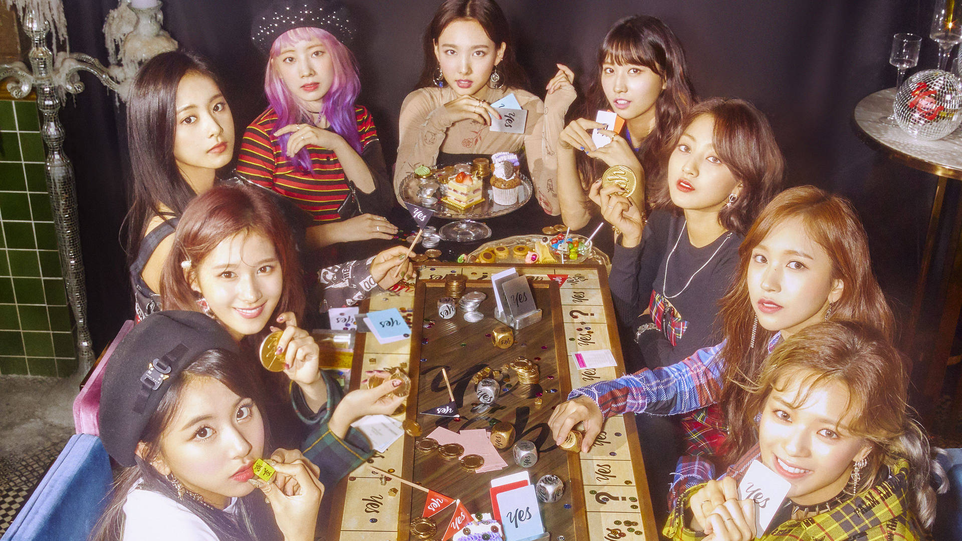 Yes or Yes 遊戲板 Twice 4K 壁紙 — 七位年輕女性穿著時尚服裝，聚集在一張充滿零食和卡片的木桌旁，房間光線昏暗，有綠色瓷磚和迪斯科球。