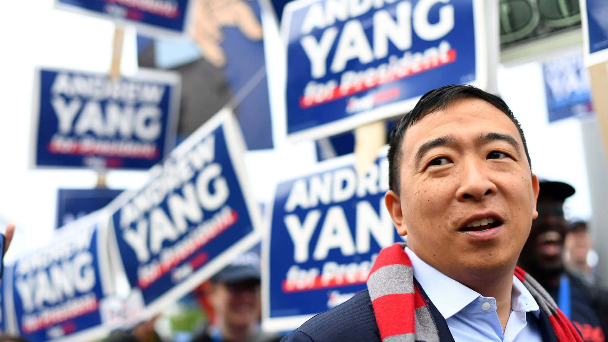 政治 桌布 壁紙 — 楊安澤在競選集會上微笑，被舉著藍色「楊安澤競選總統」標語的支持者包圍。