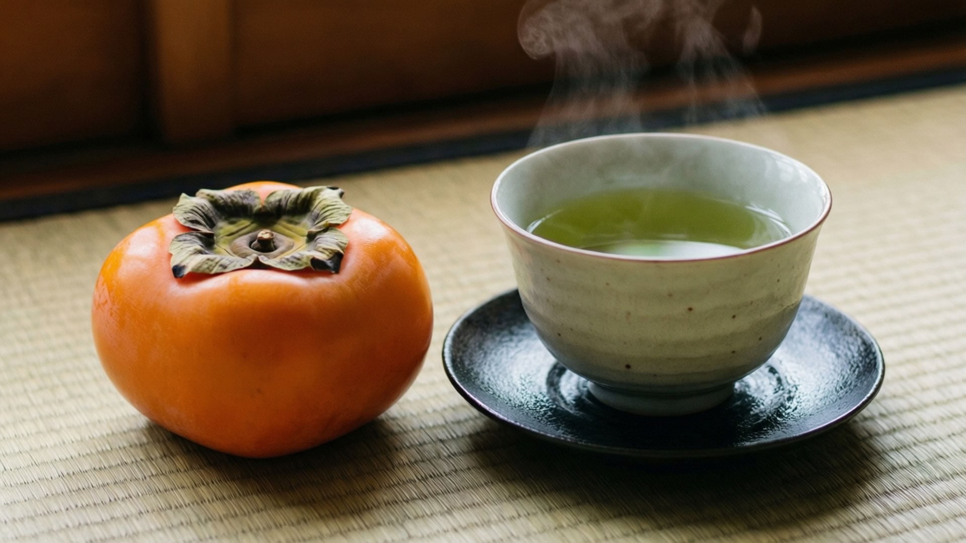 Persimmon 桌布 壁紙 — 一杯熱氣騰騰的綠茶放在一個編織榻榻米上，旁邊是一個成熟的橙色柿子，營造出寧靜的日本茶道氛圍。