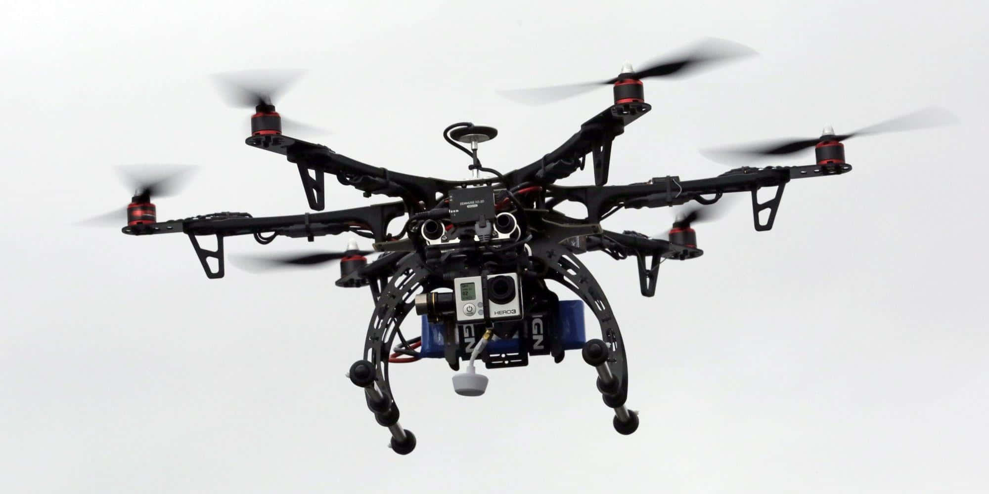 Drone Camera 桌布 壁紙 — 一部帶有紅色點綴的黑色六軸無人機，搭載攝像頭和傳感器，在蒼白的天空中盤旋。