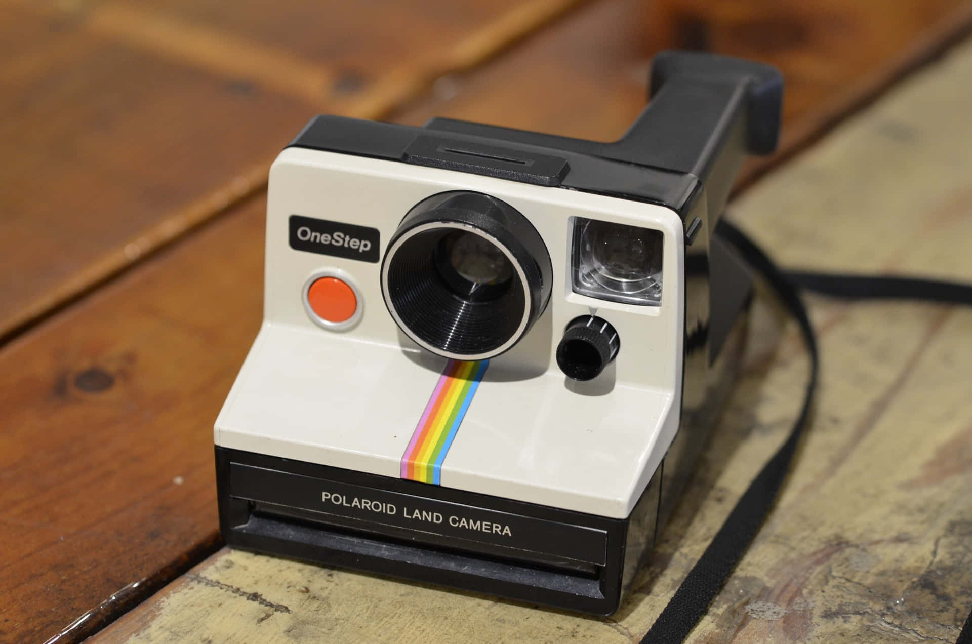  壁紙 — 一部帶有彩虹條紋的復古Polaroid OneStep相機放在風化的木質表面上。