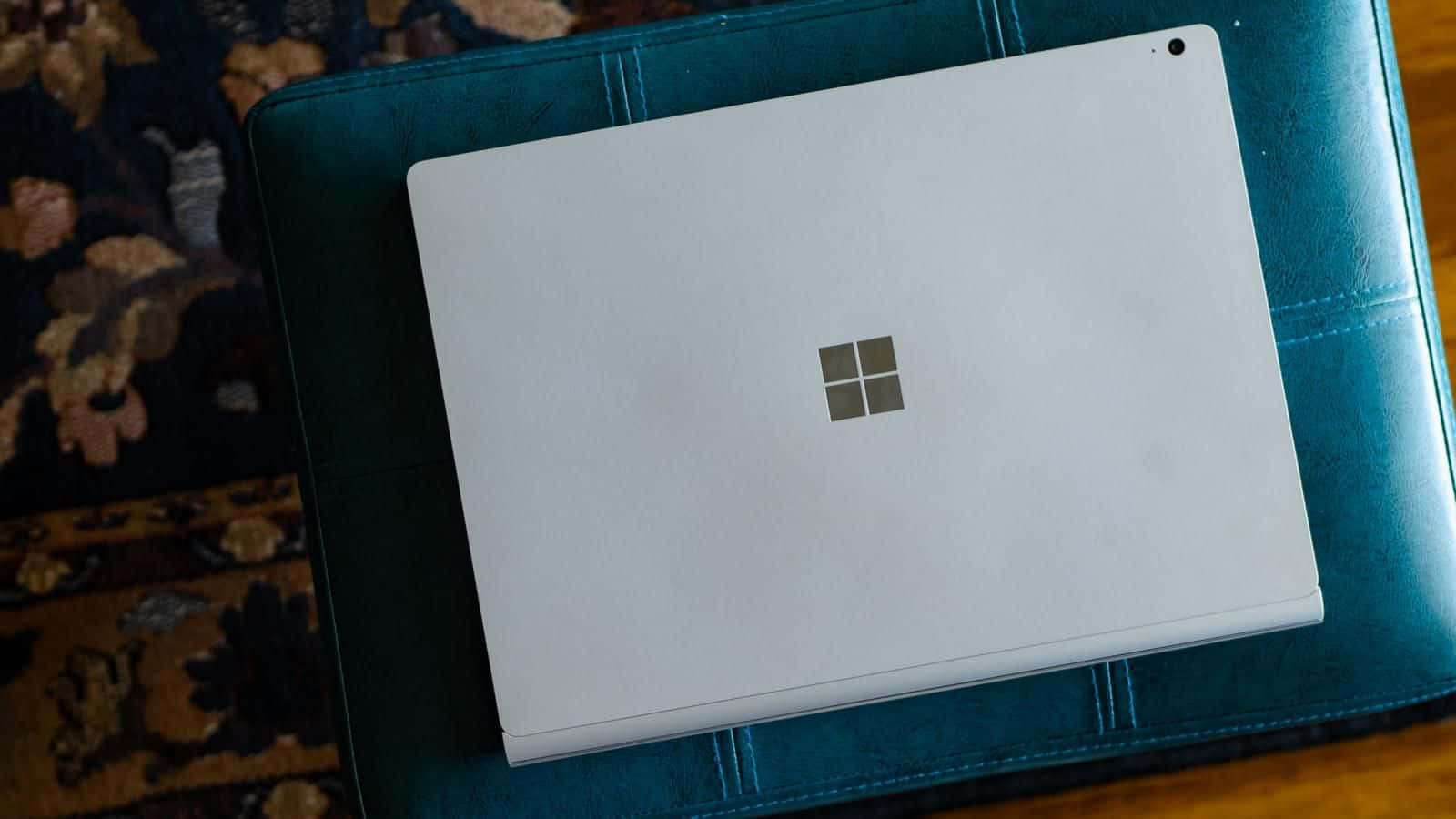  壁紙 — 一部時尚的白色Microsoft Surface平板電腦閉合地放在青綠色皮革表面上，下方鋪有圖案地毯。