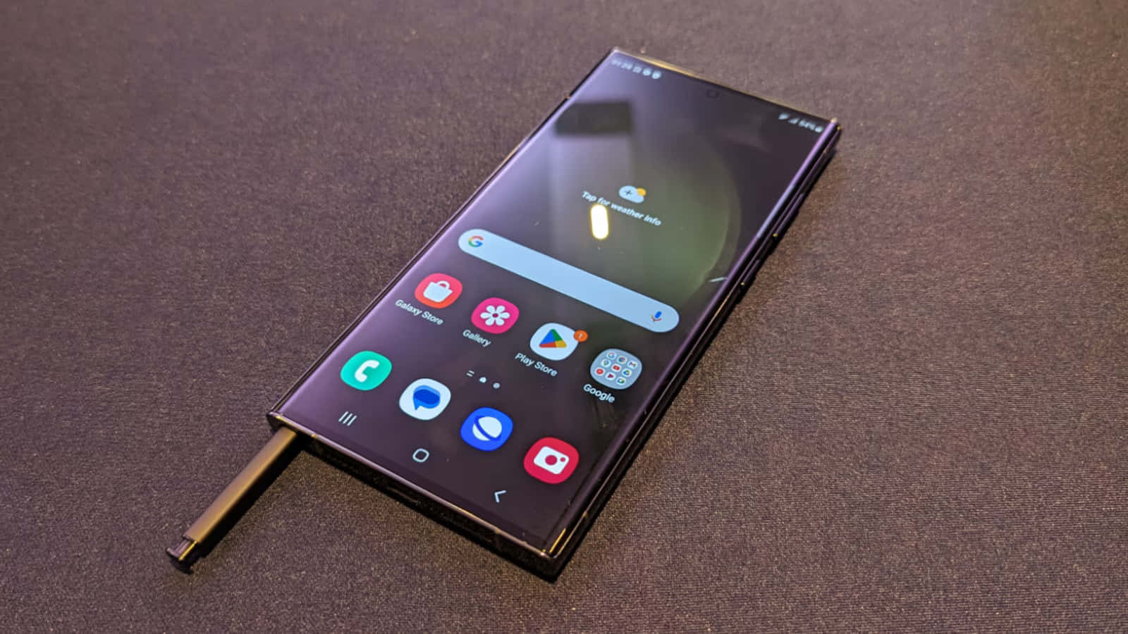 Samsung S23 Ultra 桌布 壁紙 — 一部時尚的黑色智能手機，帶有曲面屏幕和觸控筆，放置在深色紋理表面上。