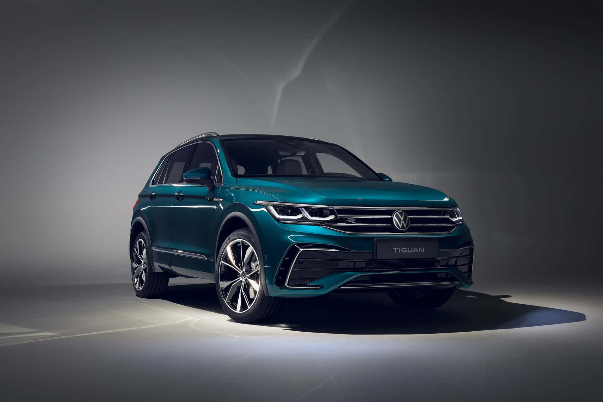  壁紙 — 一部時尚的藍綠色福士偉根 Tiguan SUV 在深灰色背景下，於戲劇性的攝影棚燈光中展示。