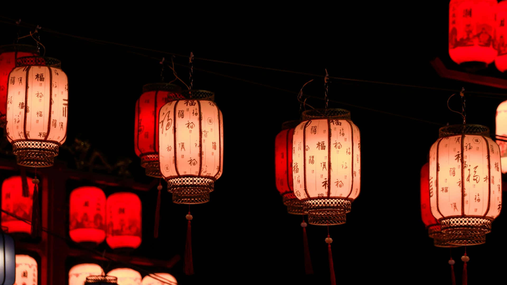  壁紙 — 一串串帶有中文字元的紅色和白色發光紙燈籠掛在漆黑的夜空下。