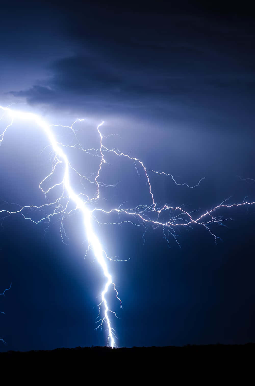 Lightning iPhone 桌布 壁紙 — 一道巨大的閃電在黑暗風暴的天空中分叉，越過剪影般的地平線。