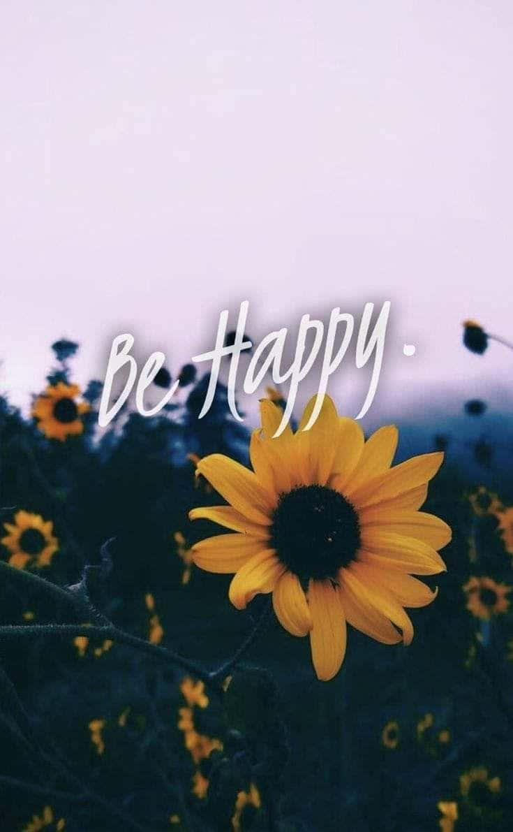 Cheerful 桌布 壁紙 — 一朵鮮豔的向日葵在柔和的紫色天空下的田野中盛開，上方優雅地寫著「Be Happy」。