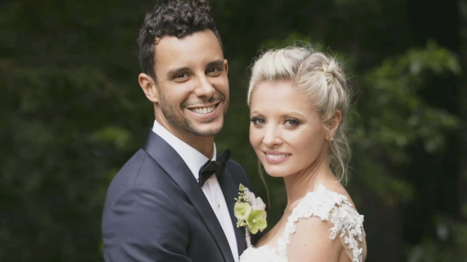 Kaitlin Doubleday 桌布 壁紙 — 一對微笑的新郎新娘穿著正式婚禮服裝，在柔和模糊的綠色樹葉背景前緊密地擺姿勢。