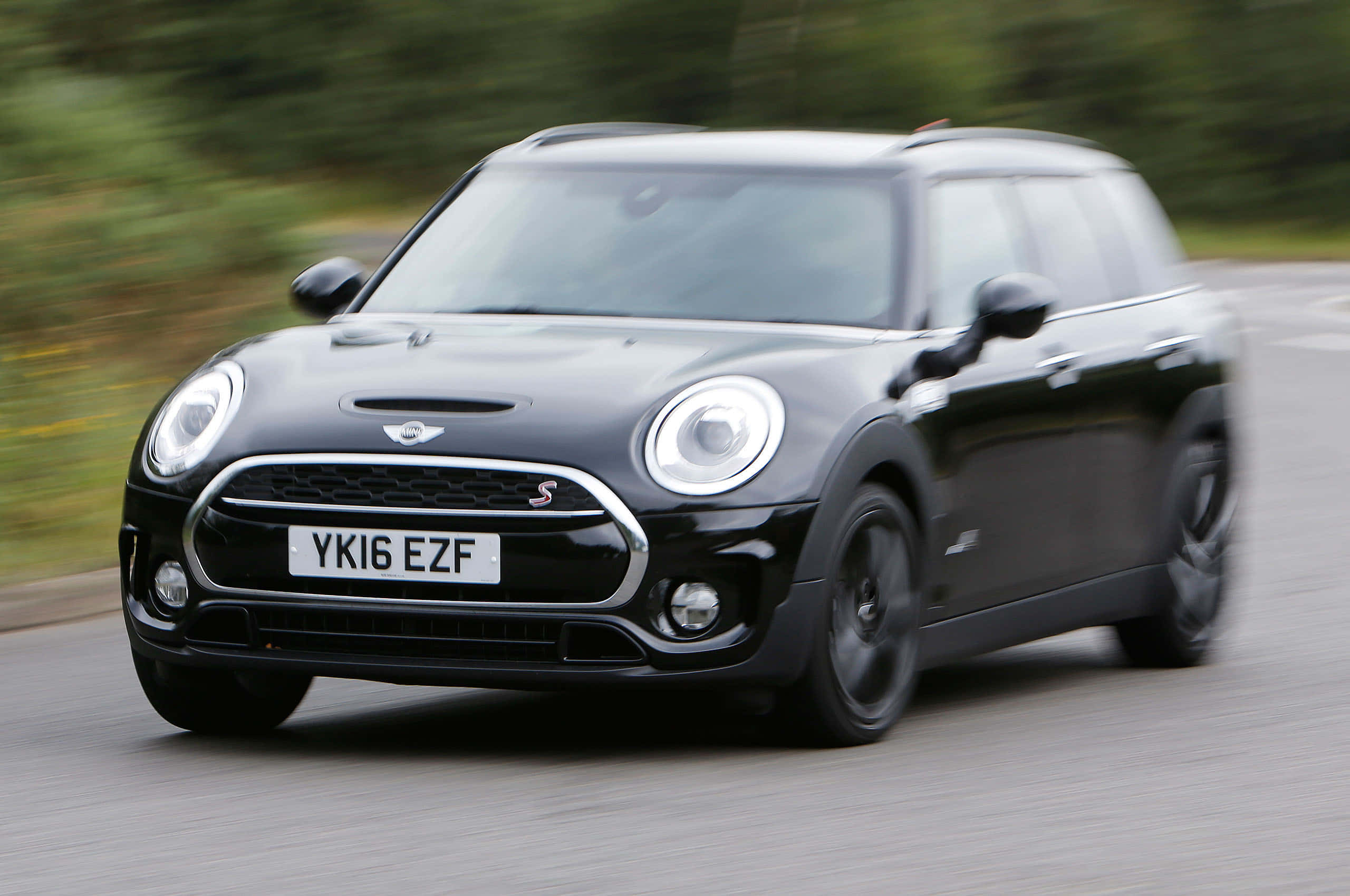 Mini Cooper S Clubman All4 桌布 壁紙 — 一架時尚的黑色MINI Countryman S在道路上飛馳，背景是模糊的綠色植物。