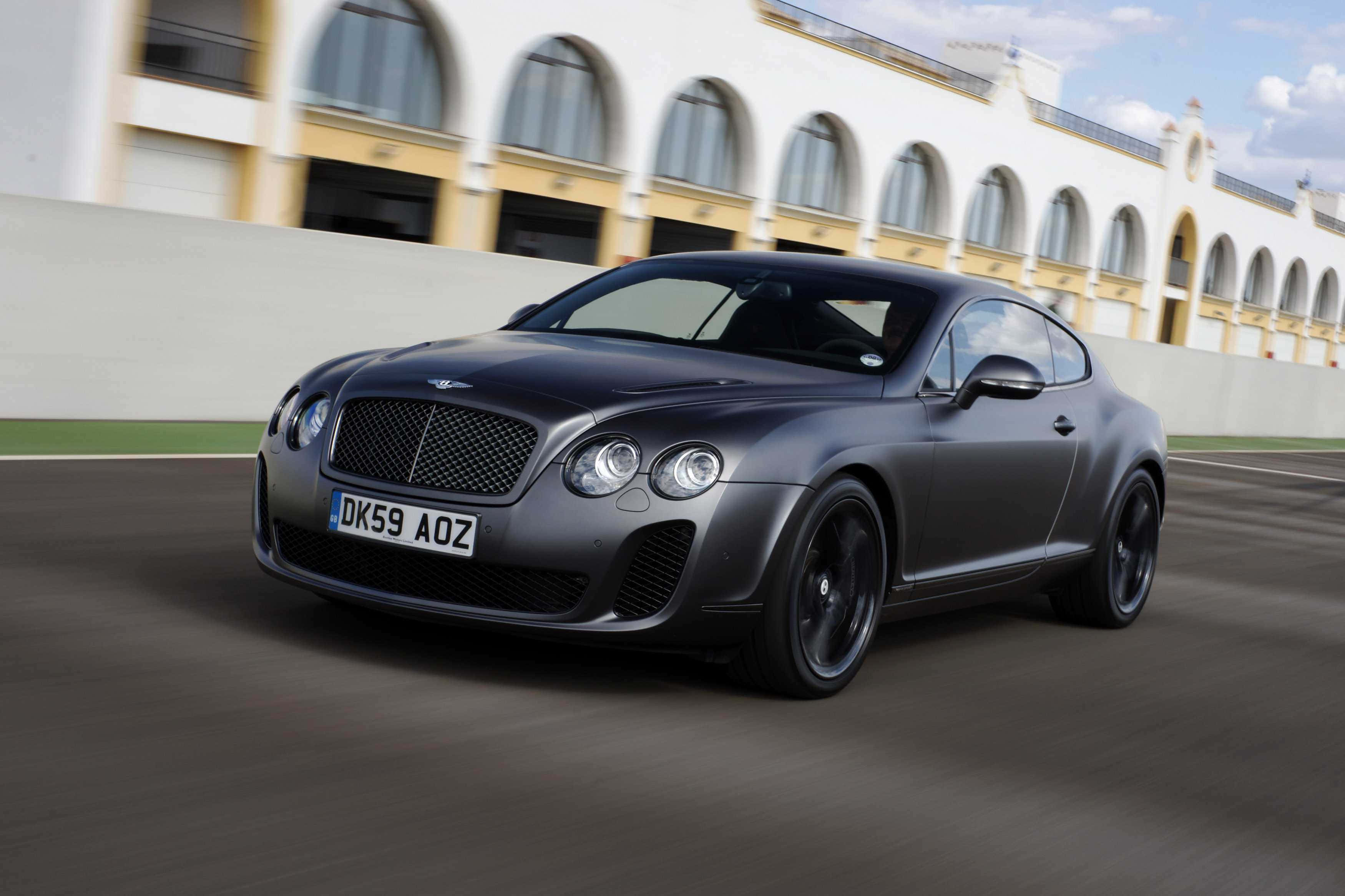 Bentley Continental Supersports 桌布 壁紙 — 一架時尚的啞光灰色 Bentley Continental GT 在賽道上飛馳，背景是一座宏偉的拱形建築。
