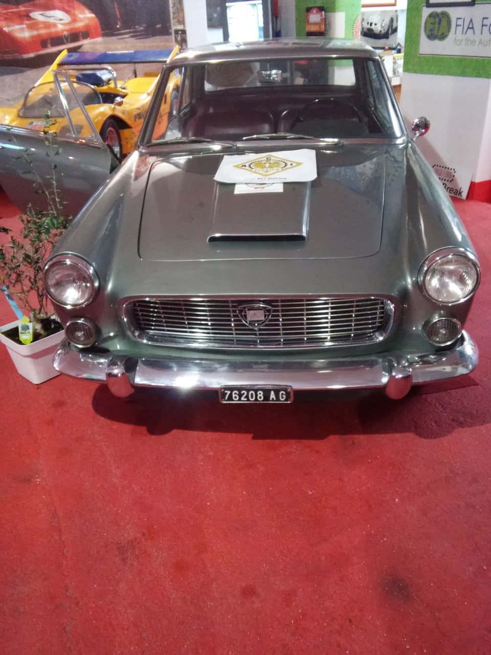  壁紙 — 一架時尚的復古綠色菲亞特124 Sport Coupe在車展的鮮紅地毯上，在明亮燈光下閃閃發光。