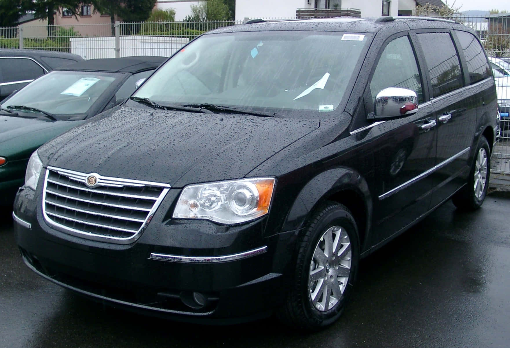 Chrysler Voyager 桌布 壁紙 — 一架時尚的黑色克萊斯勒小型貨車在陰天停泊在濕漉漉的瀝青停車場上，閃爍著雨滴。