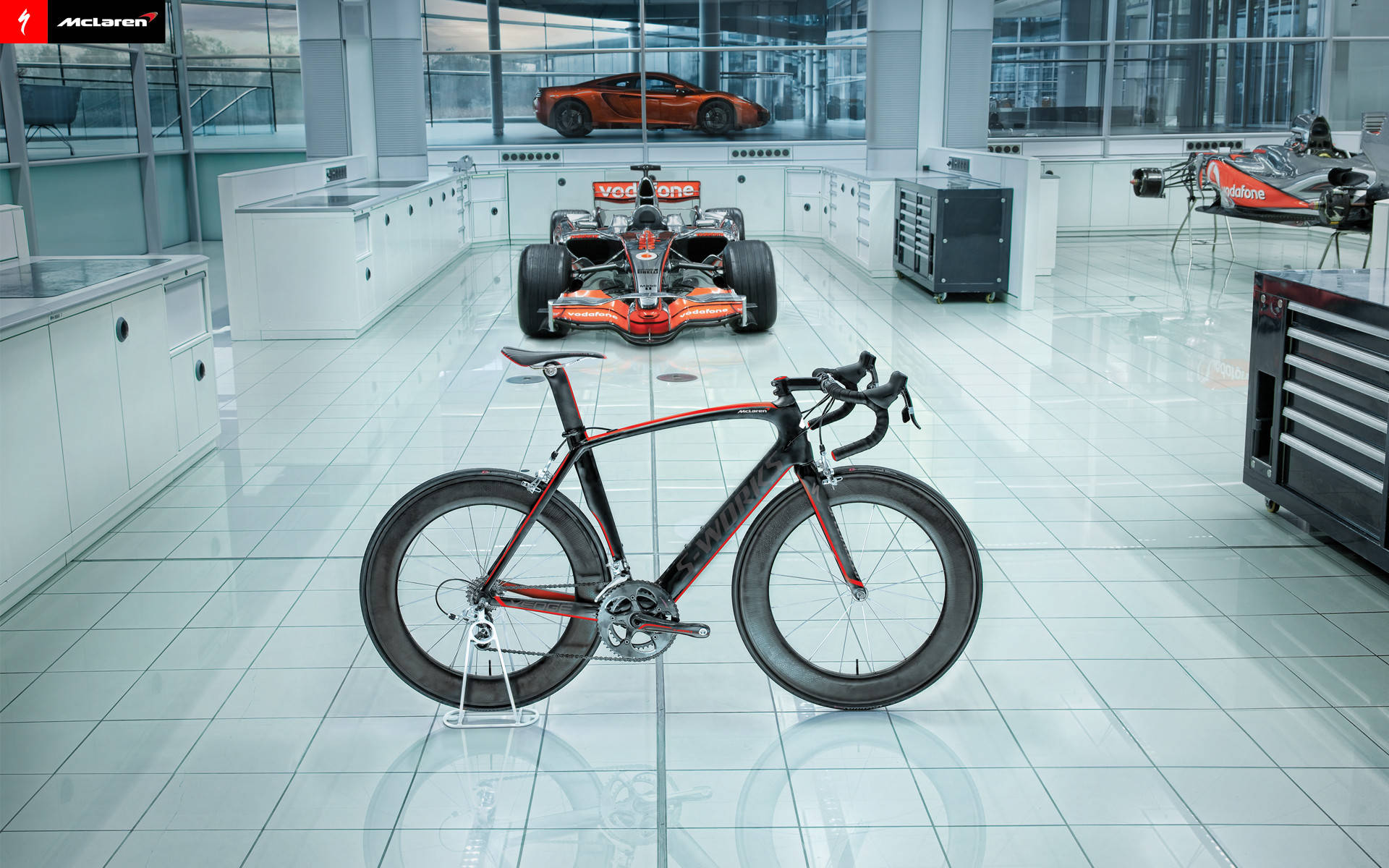 McLaren賽車單車展示於高科技車庫，背景有F1賽車和跑車。