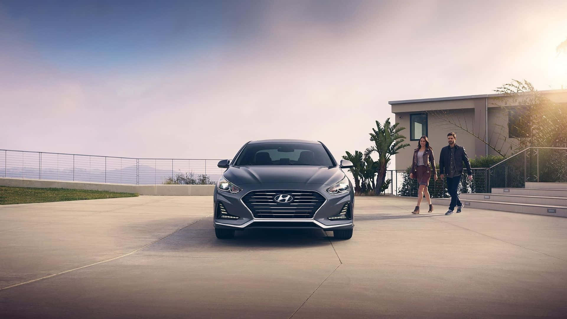 Hyundai Sonata 桌布 壁紙 — 一架時尚的灰色Hyundai房車停泊在現代化車道上，附近有一對夫婦在黃金時段於當代房屋旁散步。