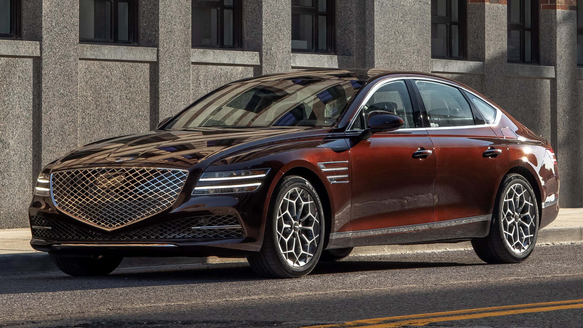 Genesis G80 桌布 壁紙 — 一架時尚的酒紅色Genesis G90轎車在明亮的陽光下閃閃發光，停泊在灰色石建築旁的街道上。