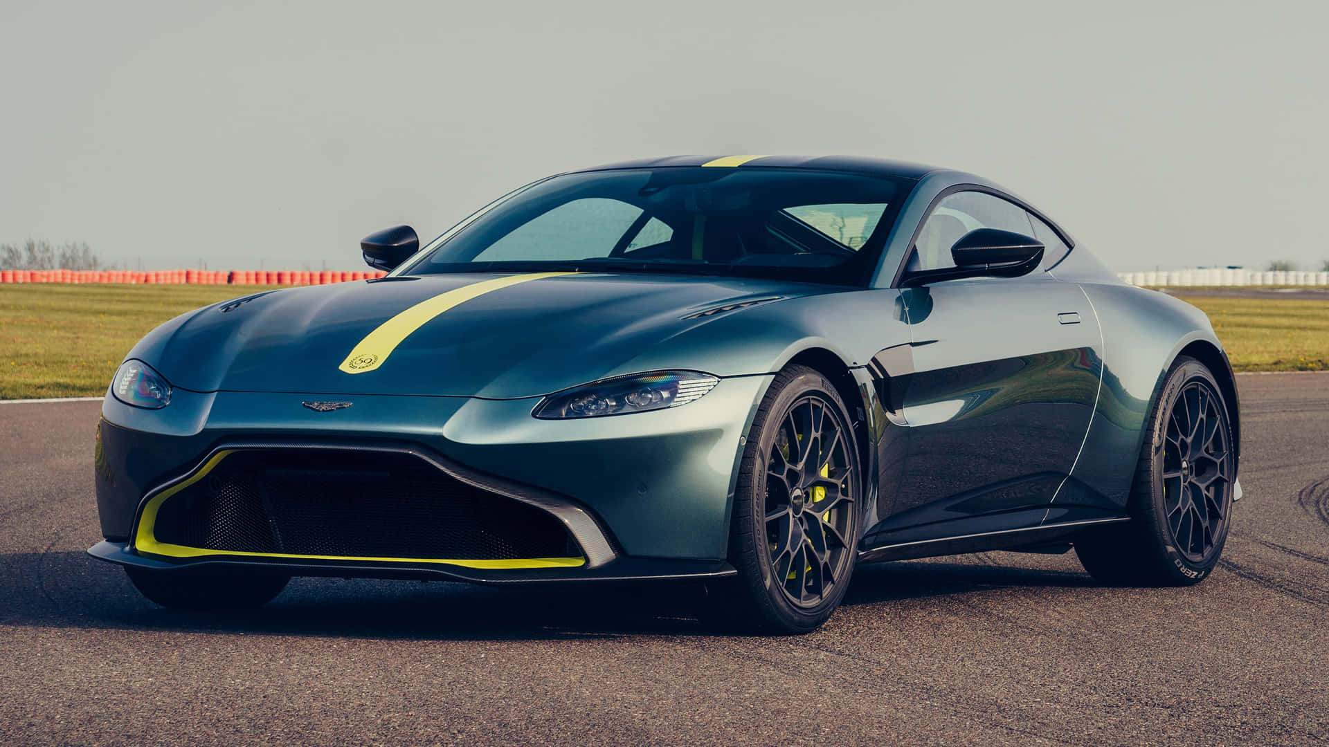 Aston Martin Vantage 桌布 壁紙 — 一架時尚金屬綠色 Aston Martin 跑車，帶有醒目的黃色賽車條紋，停在賽道上。