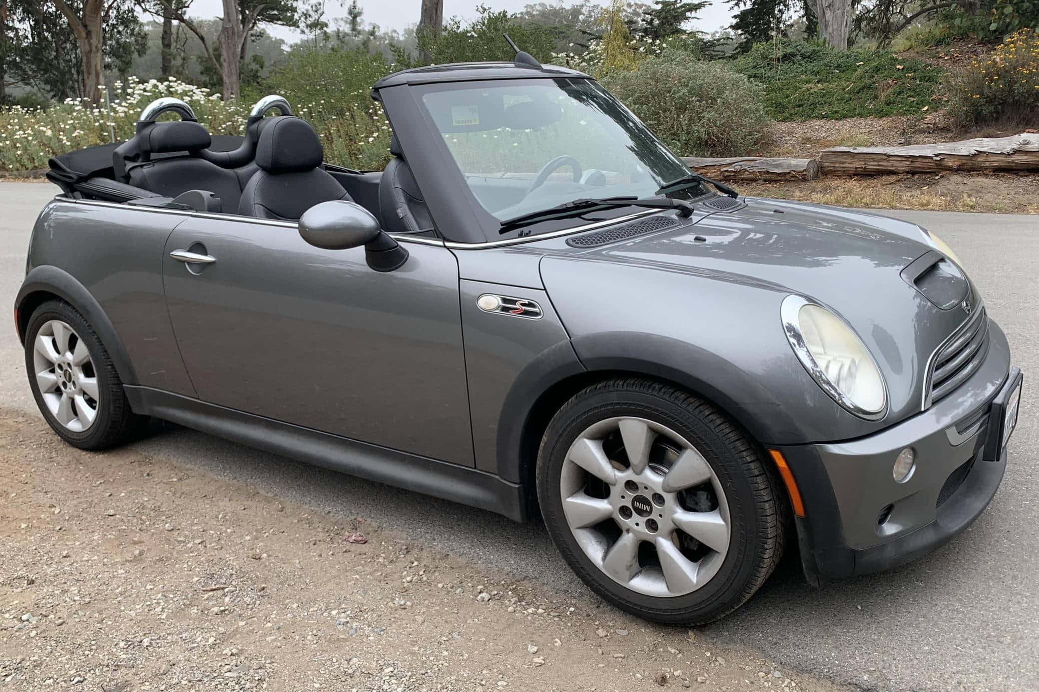 Mini Cooper Convertible 桌布 壁紙 — 一架時尚的灰色開篷跑車停泊在碎石路上，背景有樹木和野花。