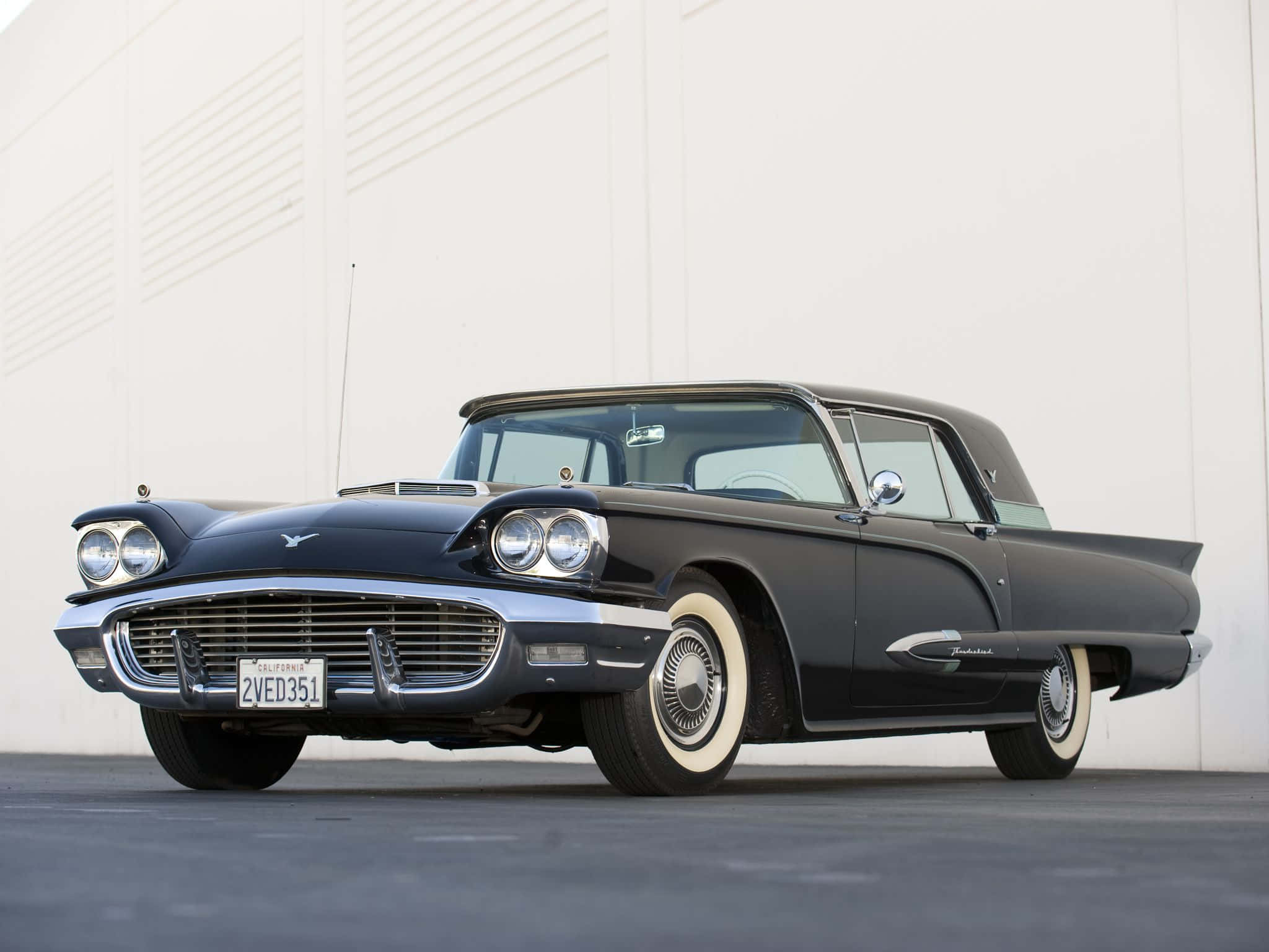 Ford Thunderbird 桌布 壁紙 — 一架時尚的黑色1957年福特雷鳥經典車，配備白邊輪胎，停放在簡約的白色牆壁前。