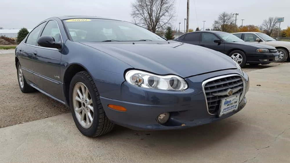 Chrysler Lhs 桌布 壁紙 — 一架時尚的藍色 Chrysler 房車停在碎石停車場，背景有光禿的樹木和陰天。