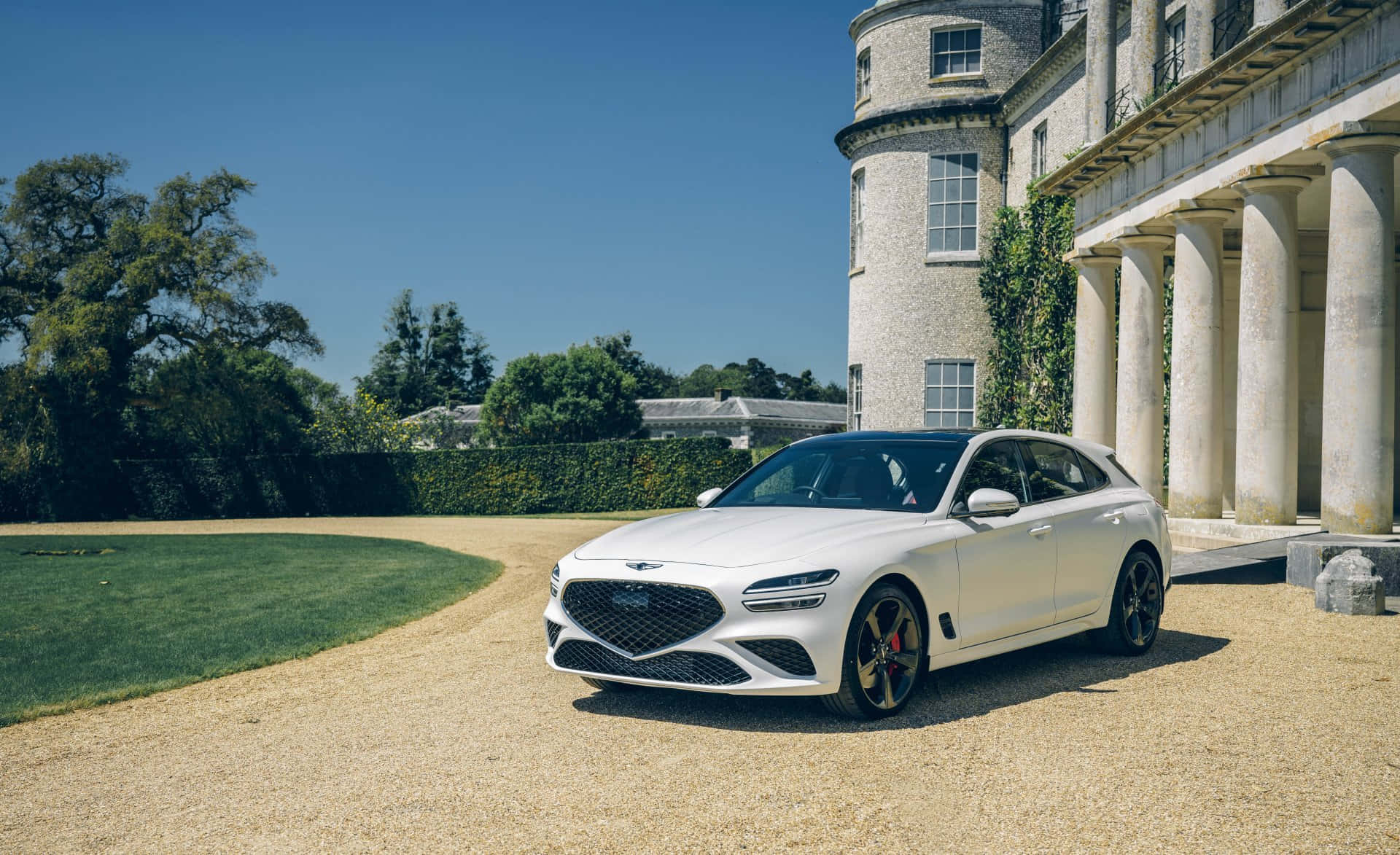 Genesis G70 桌布 壁紙 — 一架時尚的白色豪華SUV停泊在碎石路上，前方是一座宏偉的石砌大宅，有柱子和常春藤，天空清澈湛藍。