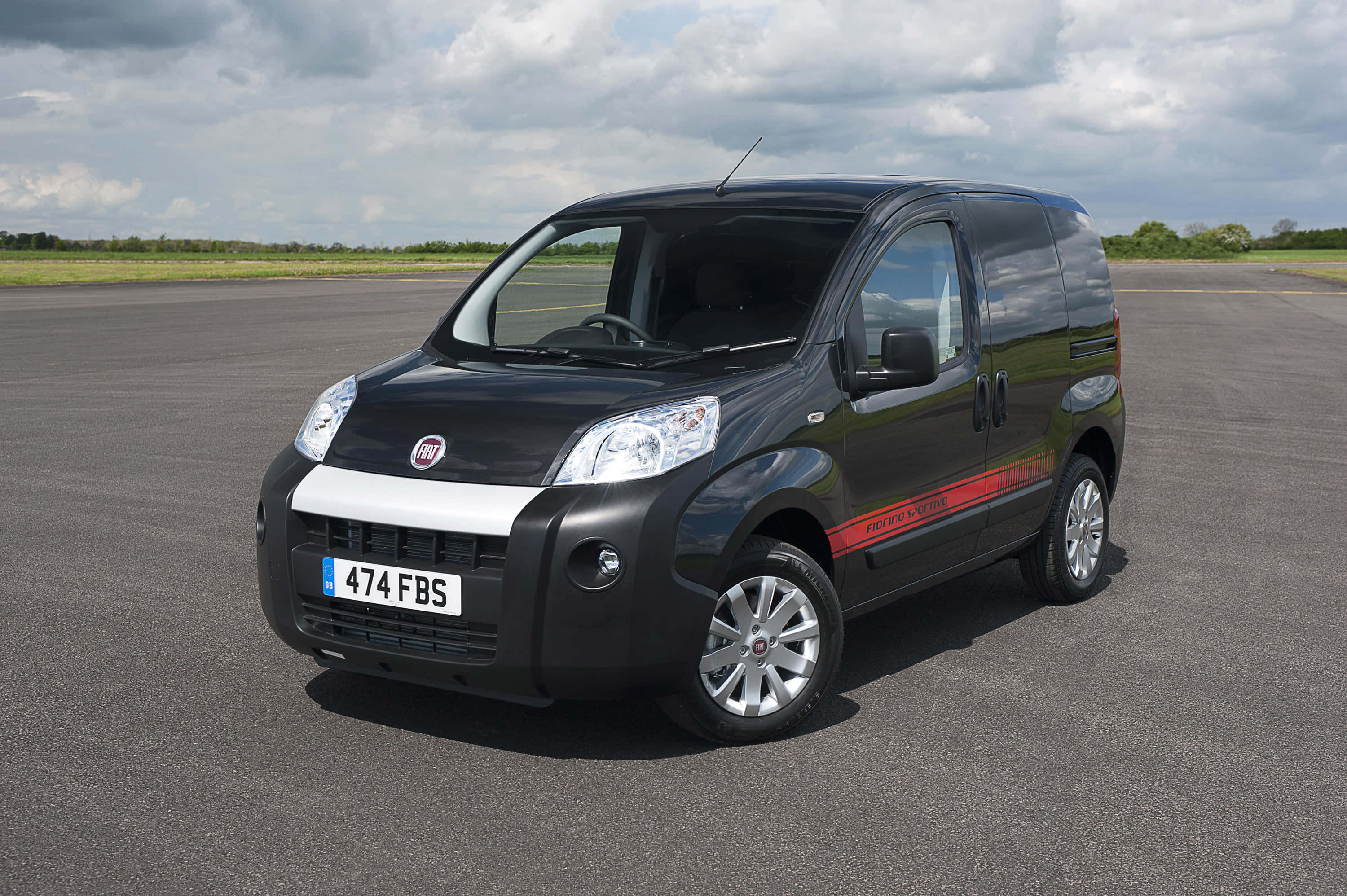Fiat Fiorino 桌布 壁紙 — 一架時尚黑色菲亞特 Fiorino 客貨車，帶有紅色賽車條紋，停泊在陰天下一條寬闊的瀝青跑道上。