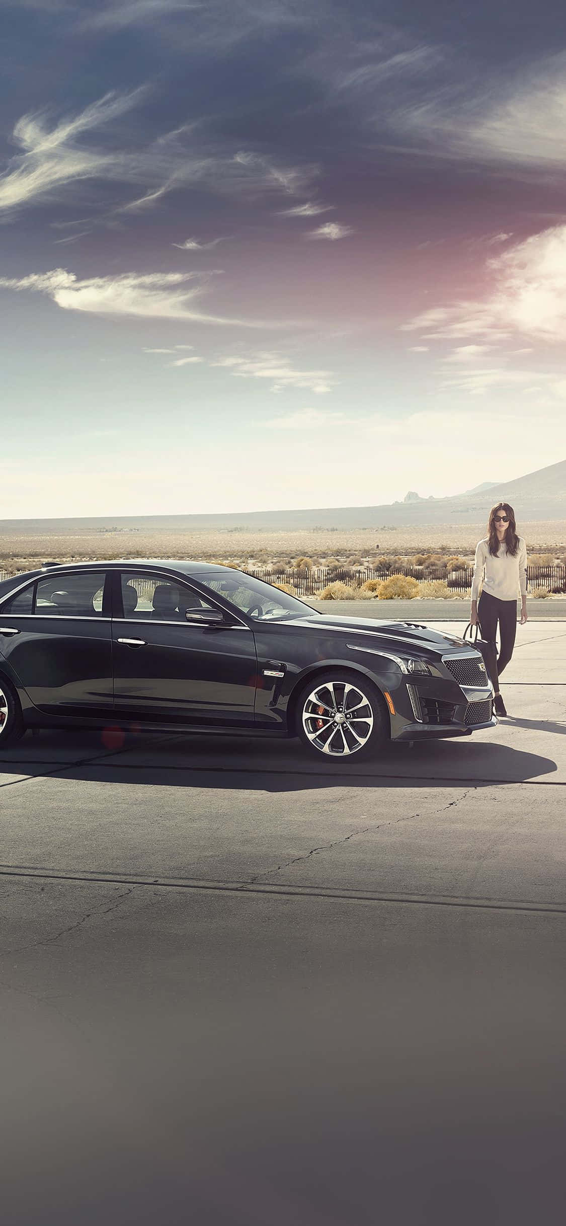 Cadillac Cts 桌布 壁紙 — 一架時尚黑色豪華轎車停在沙漠公路上，一名女子站在車旁，背景是戲劇性的暮色天空。