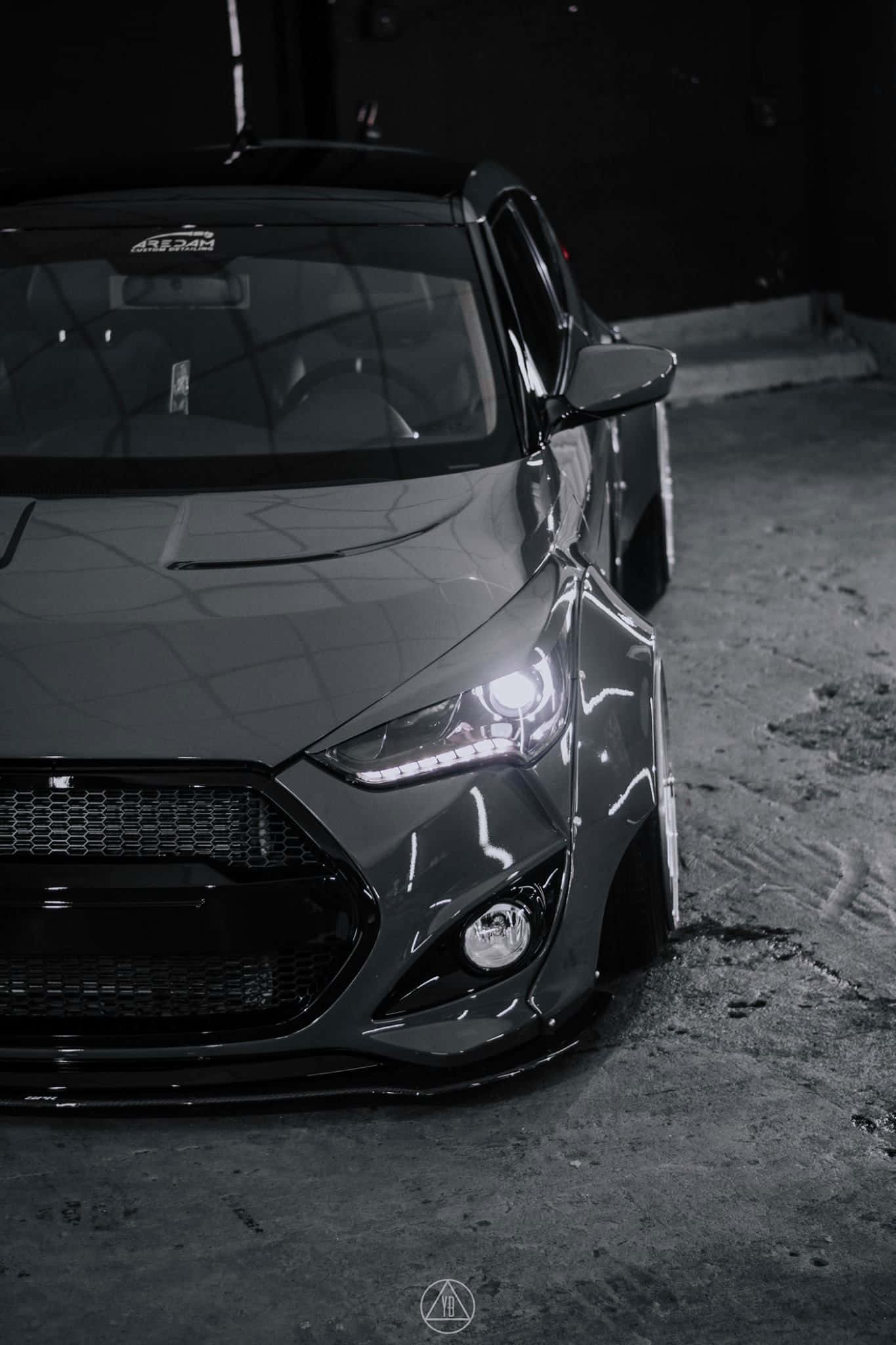 Hyundai Veloster 桌布 壁紙 — 一架時尚灰色改裝車，車頭燈發光，停在光線昏暗的混凝土車庫中。
