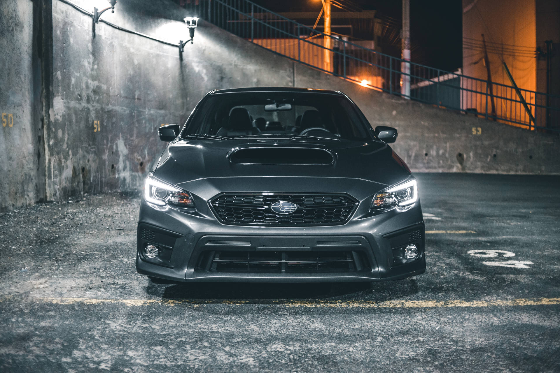一架黑色Subaru WRX STI停泊在黑暗的市區車庫，車頭燈亮著。