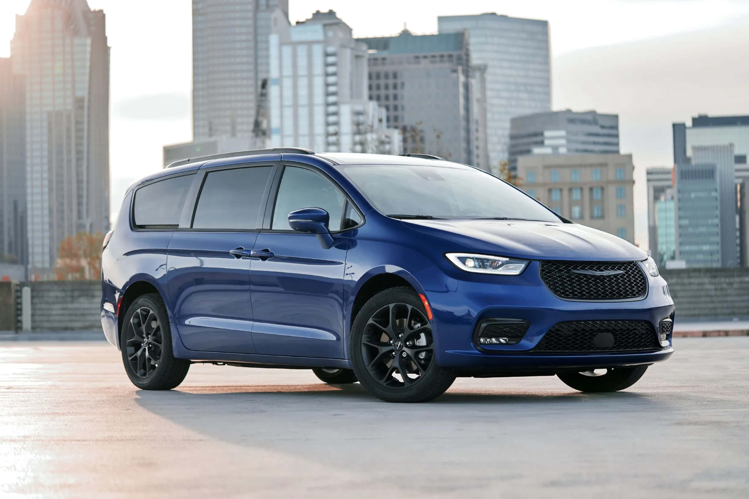 Chrysler Pacifica 桌布 壁紙 — 一架時尚的藍色小型貨車停泊在天台上，背景是現代城市天際線。
