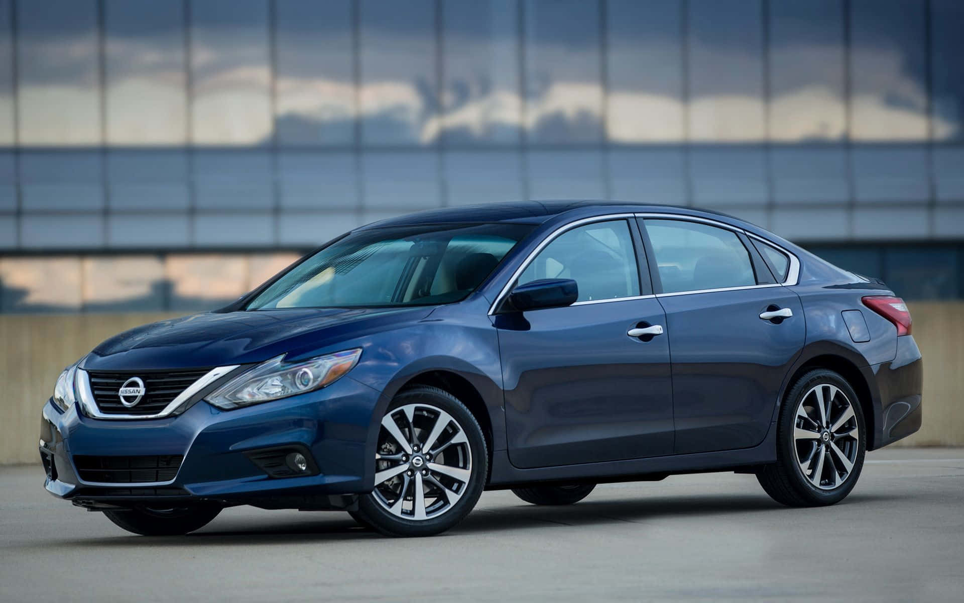 Nissan Altima 桌布 壁紙 — 一架時尚的藍色日產房車停泊在現代玻璃建築前，天空多雲。