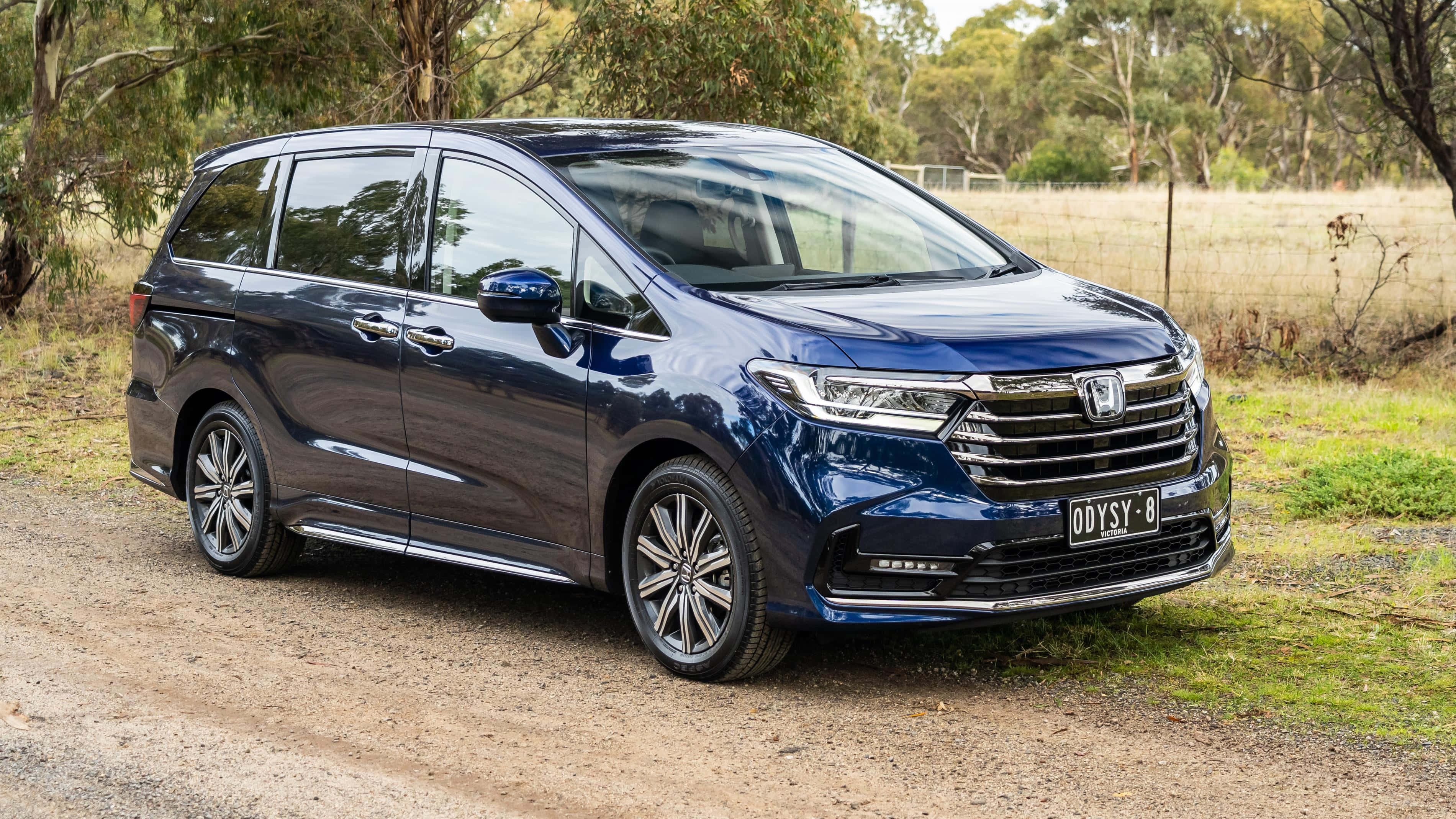 Honda Odyssey 桌布 壁紙 — 一架時尚的藍色本田Odyssey小型貨車停泊在泥路上，周圍環繞著樹木和草地。