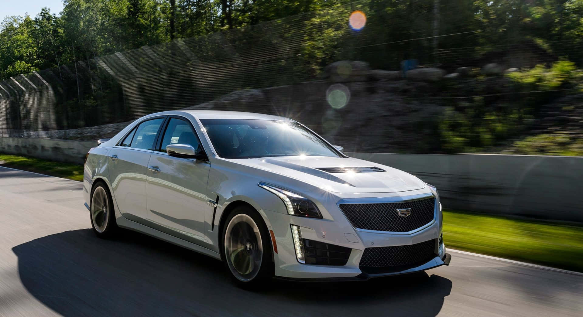 Cadillac Cts 桌布 壁紙 — 一架時尚的銀色Cadillac CTS-V在陽光明媚的賽道上疾馳，背景是模糊的綠化和石牆。