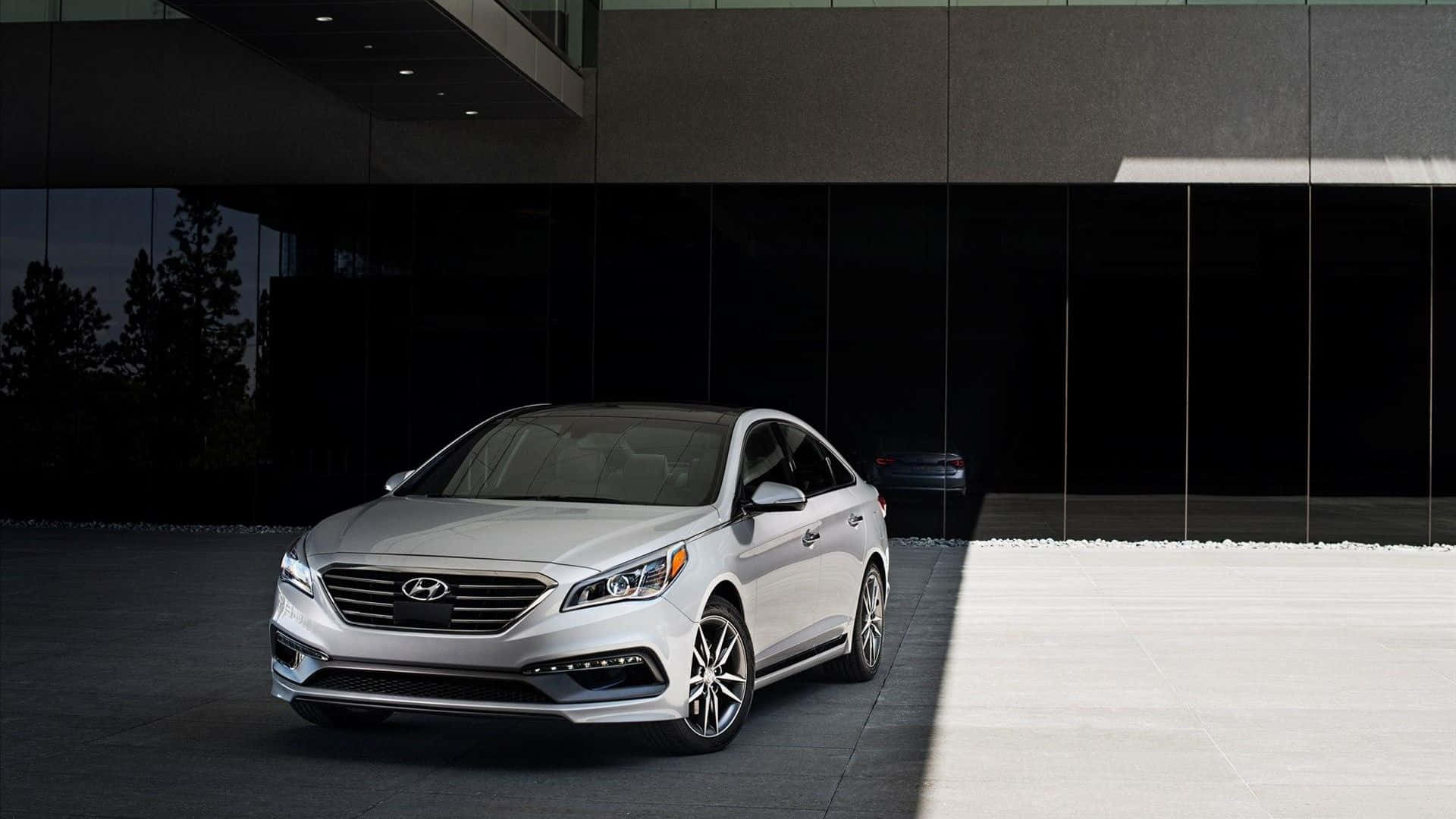 Hyundai Sonata 桌布 壁紙 — 一架時尚的銀色轎車停在一棟現代玻璃建築前，燈光效果戲劇化。
