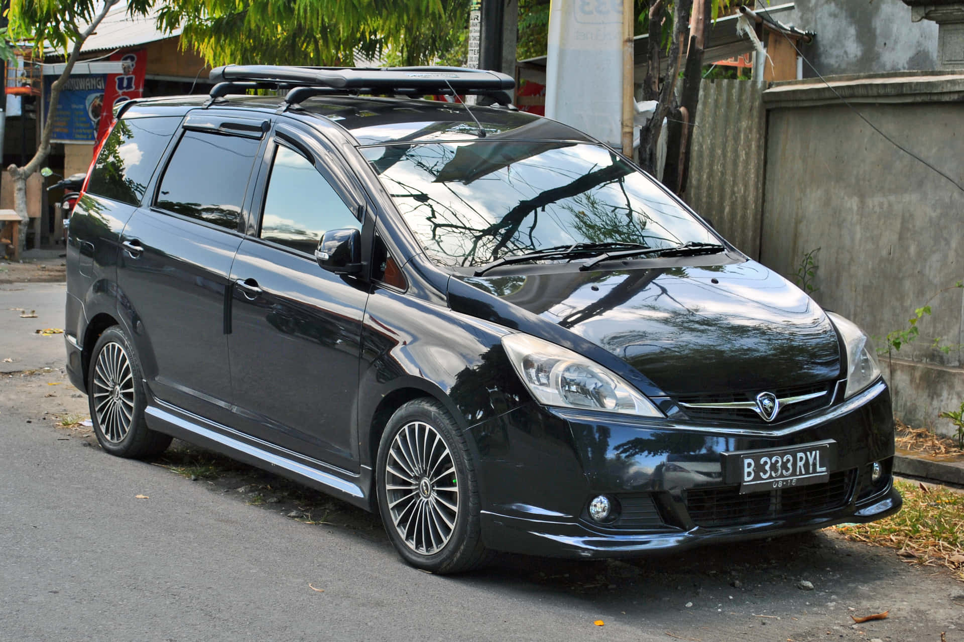 黑色小型貨車配備車頂行李架，停泊在種有樹木和建築物的城市街道上。 — 美學白色動態圖 壁紙