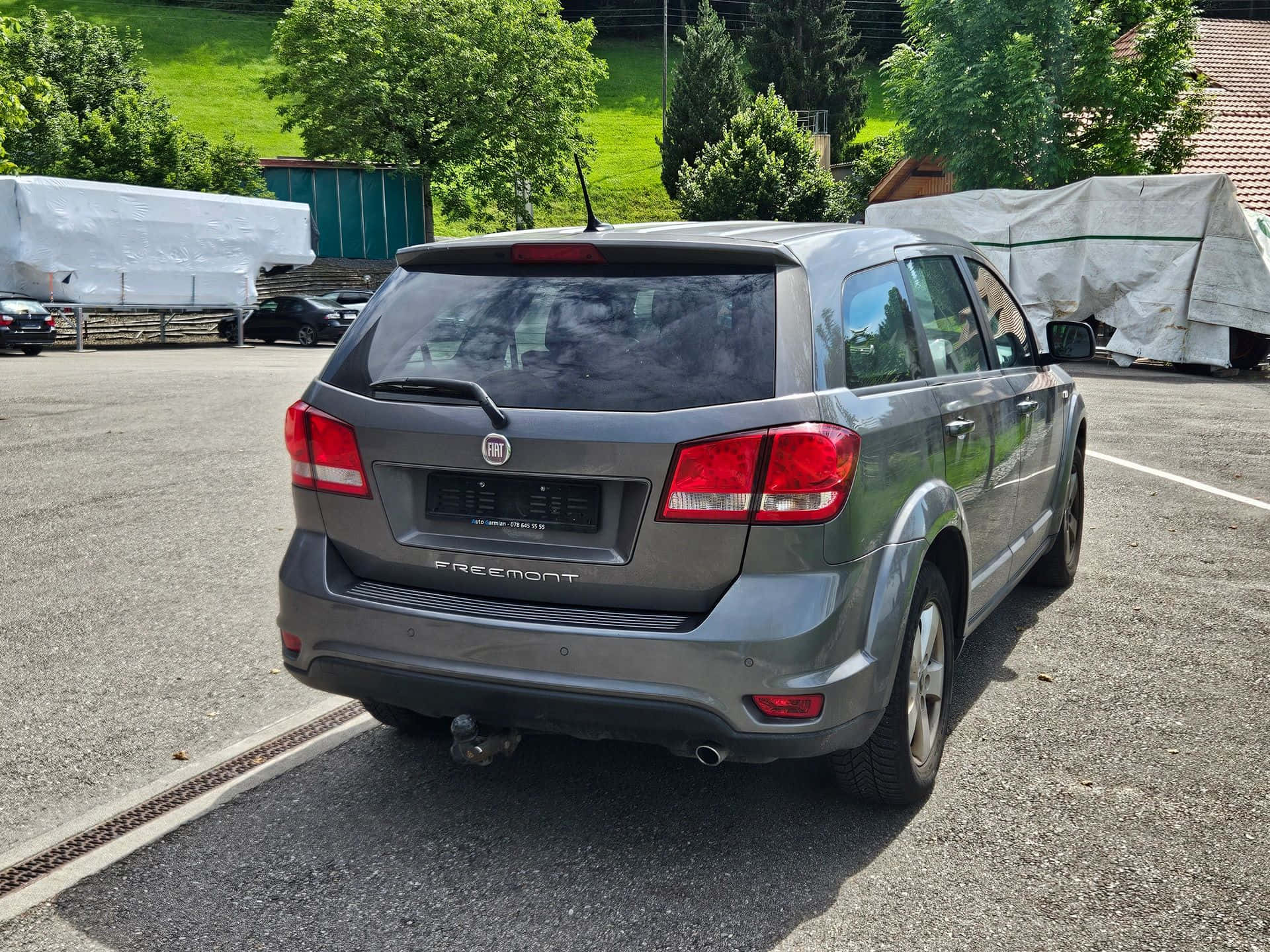  壁紙 — 一架灰色 Fiat Freemont SUV 停泊在陽光普照的停車場，背景有綠色山丘和樹木。