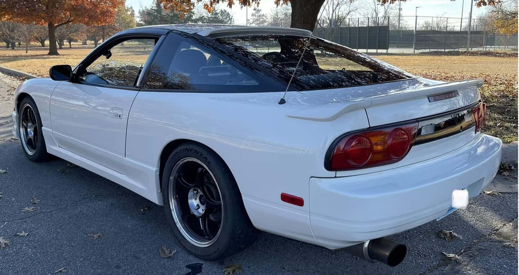  壁紙 — 一架純白色的日產Skyline R33 GT-R停泊在落葉滿佈的瀝青停車場，背景是秋天的樹木。