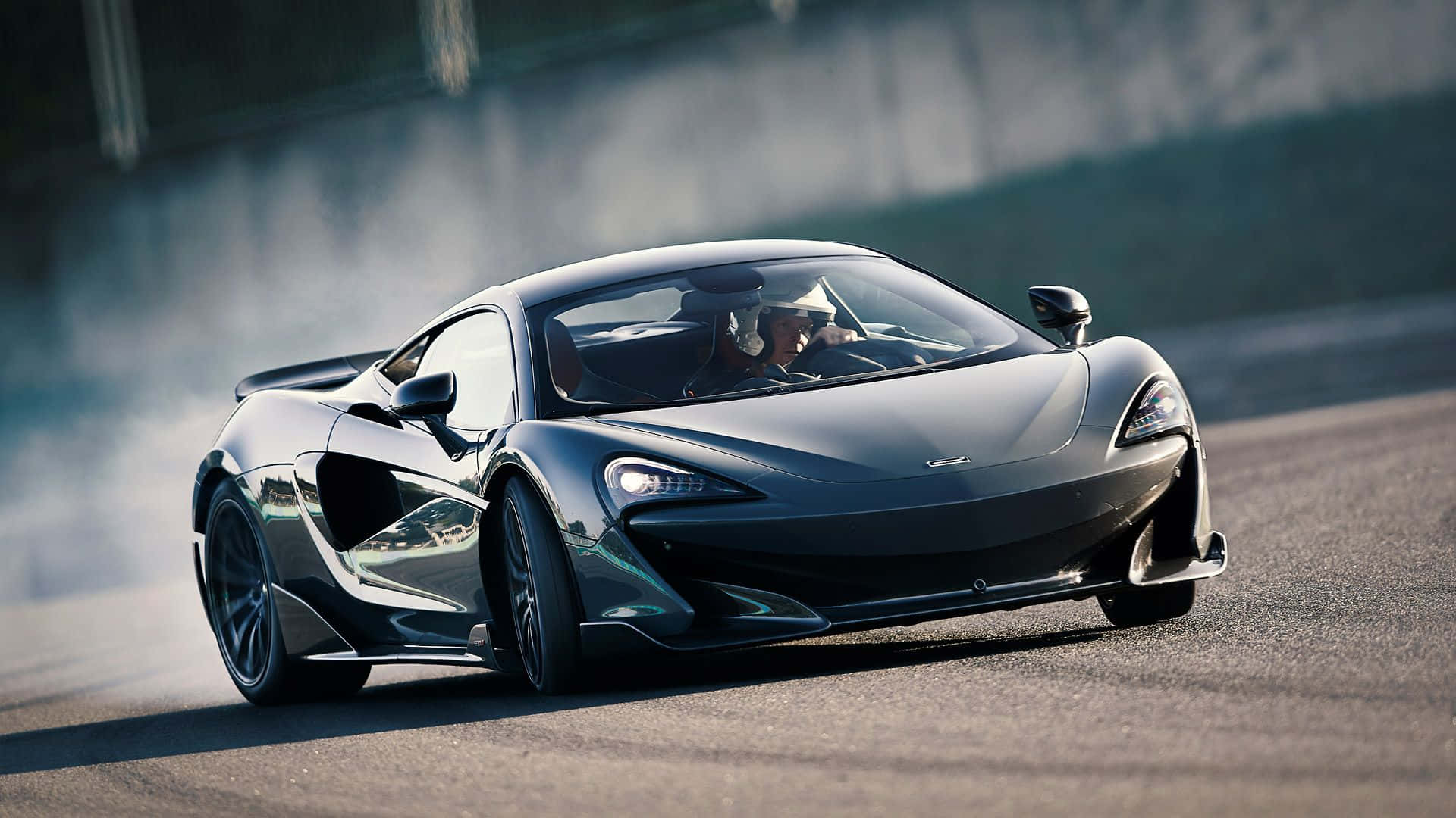 Mclaren 600lt 桌布 壁紙 — 一架時尚的黑色McLaren跑車在賽道上飄移，輪胎在明亮的日光下冒出滾滾濃煙。