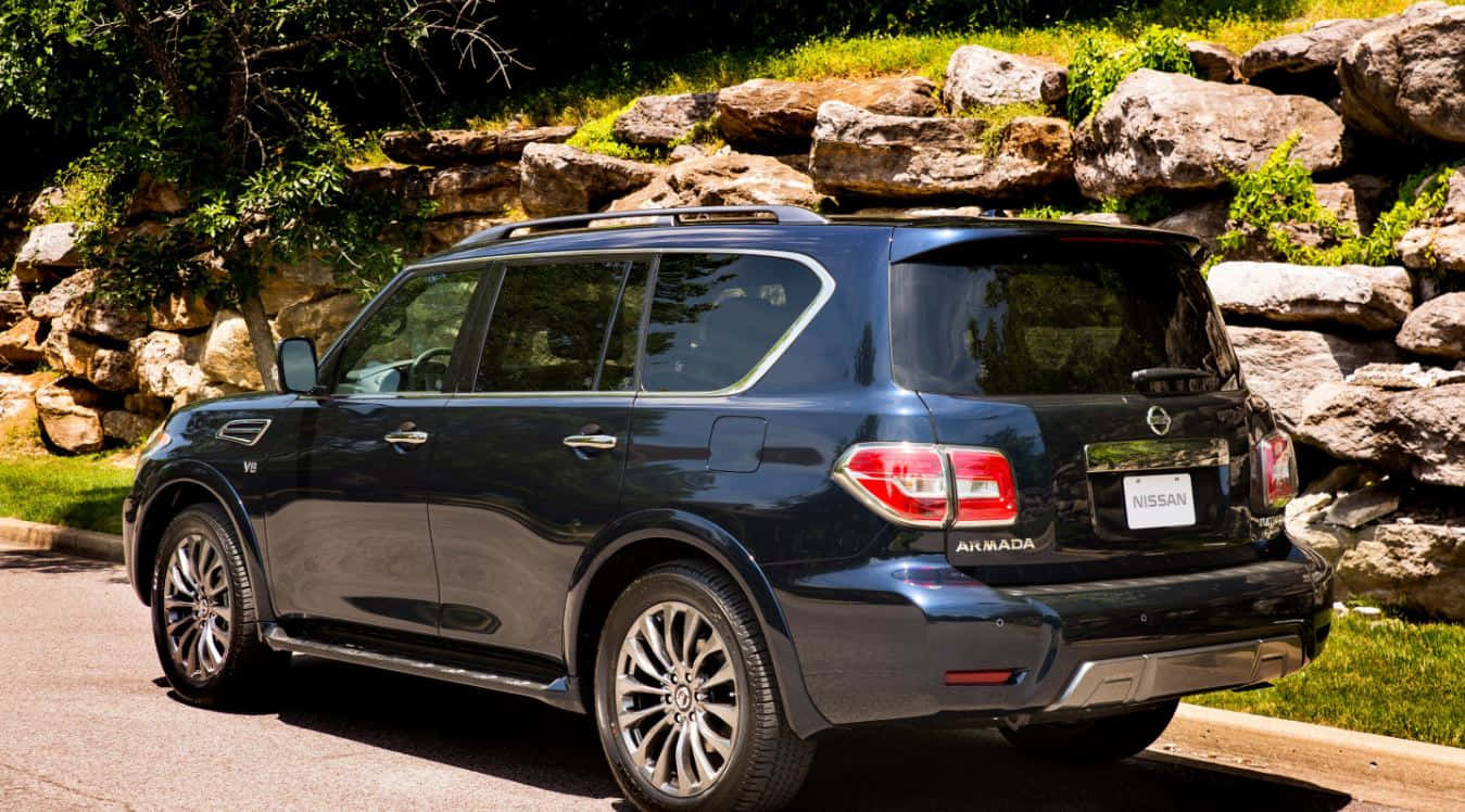 Nissan Armada 桌布 壁紙 — 一架時尚的黑色日產Armada SUV停泊在鋪砌道路上，旁邊是陽光照射的石牆和綠草。