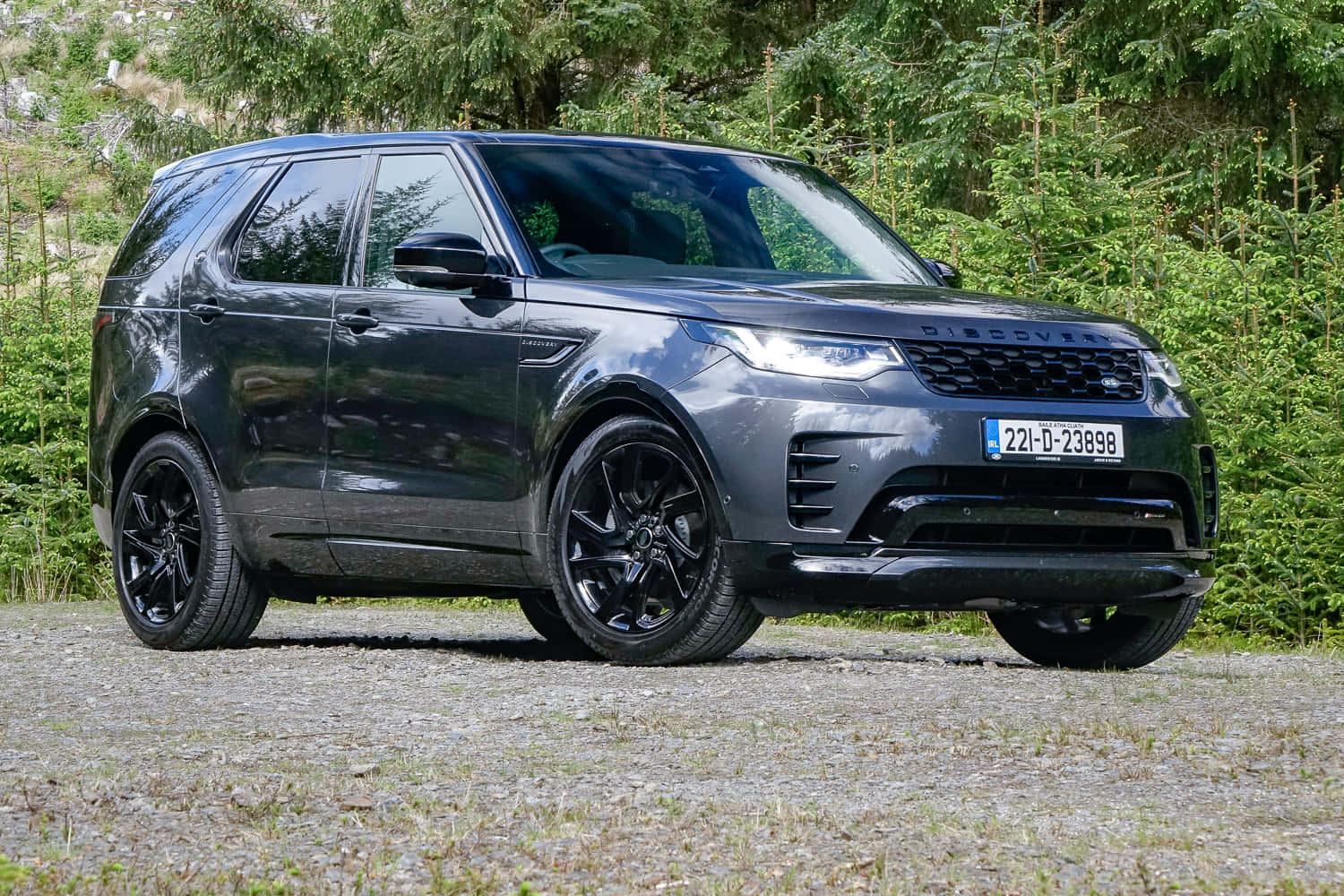 Land Rover Discovery 桌布 壁紙 — 一架時尚的啞光灰色 Land Rover Discovery 停在碎石路上，背後是茂密的綠色森林。