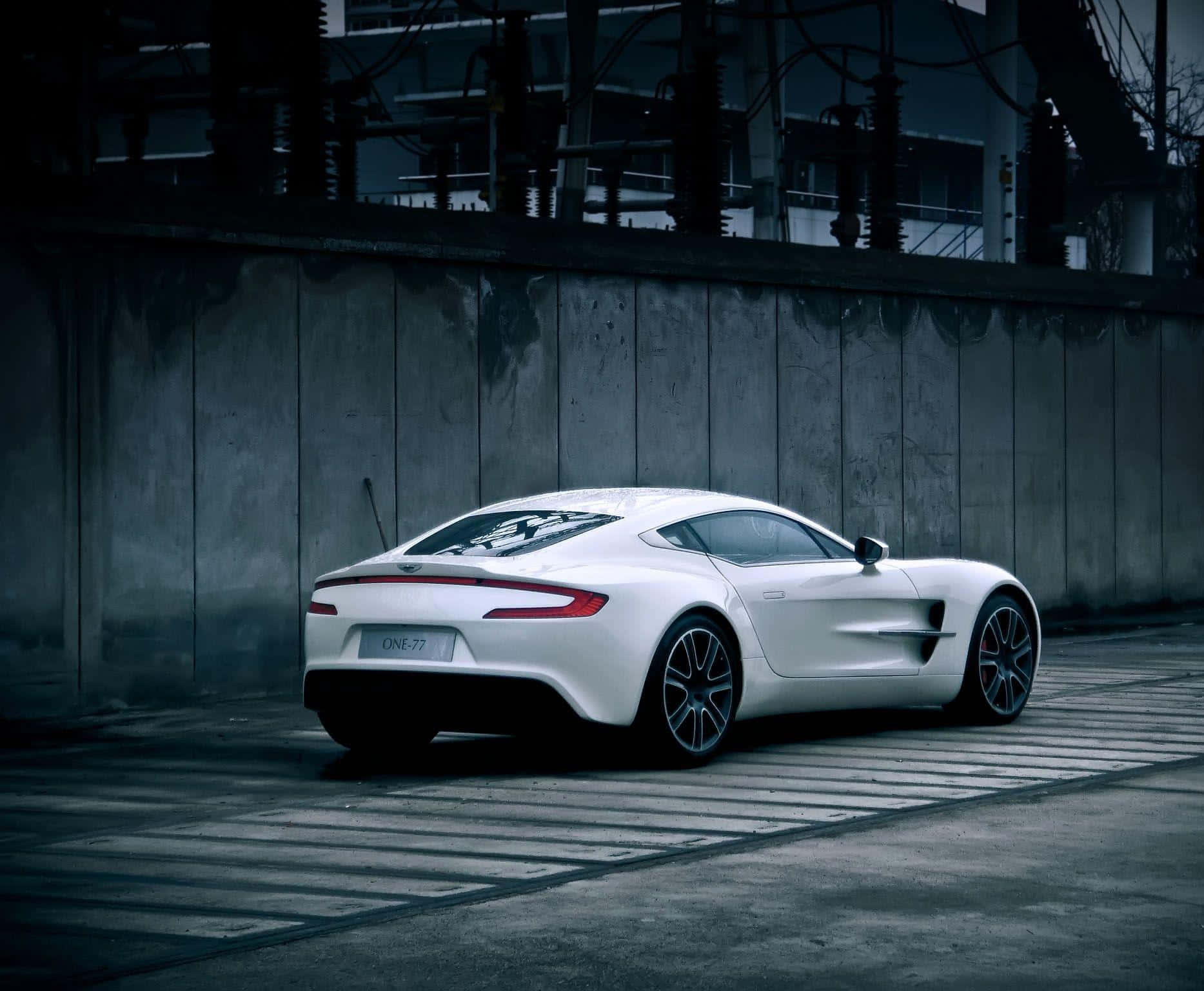 Aston Martin One-77 桌布 壁紙 — 一架時尚的白色Aston Martin One-77跑車停在混凝土表面上，旁邊是風化的工業牆，光線昏暗。
