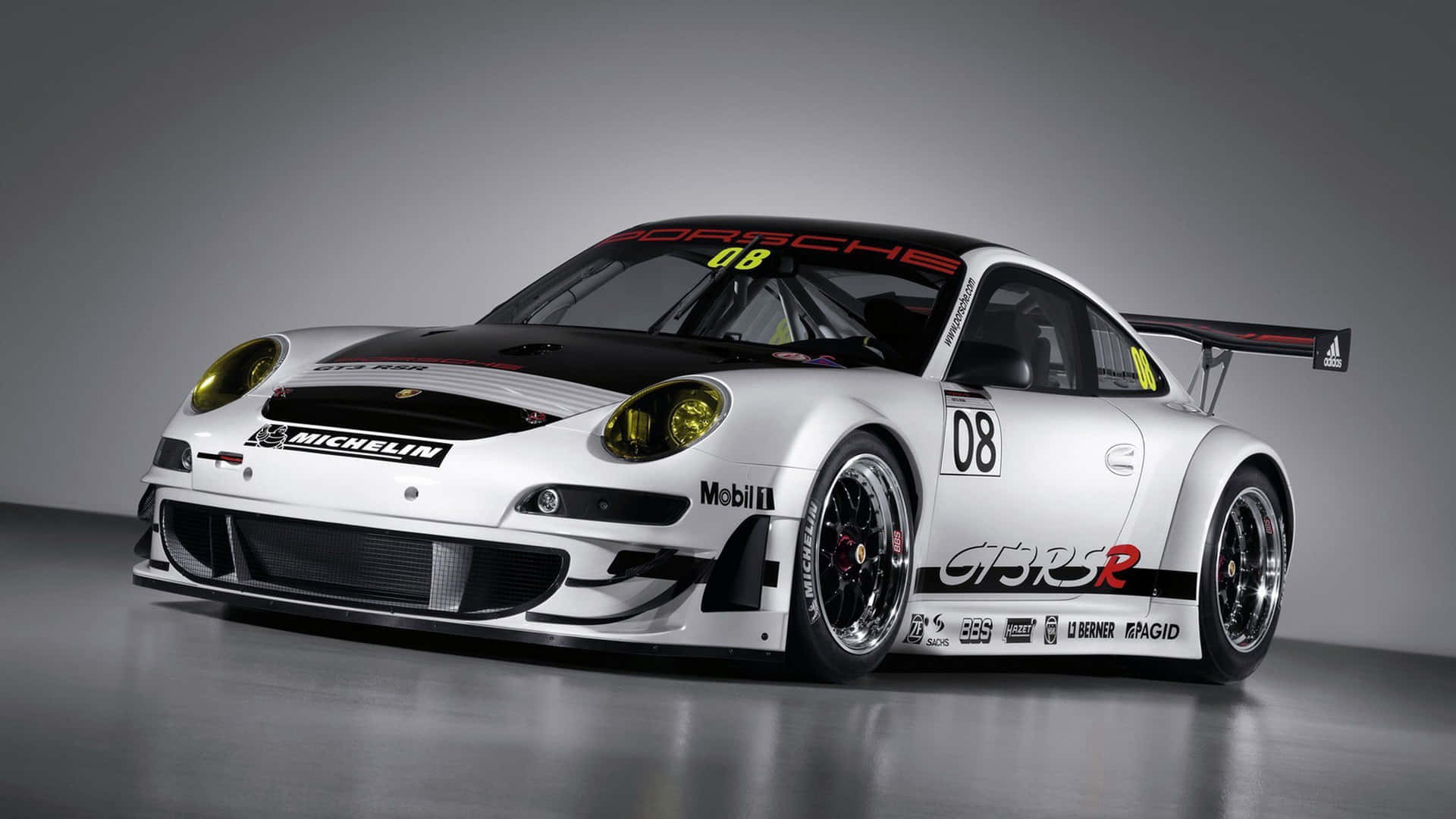白色保時捷911 GT3 R賽車，帶有黑色飾件和贊助商標誌，在攝影棚中。
