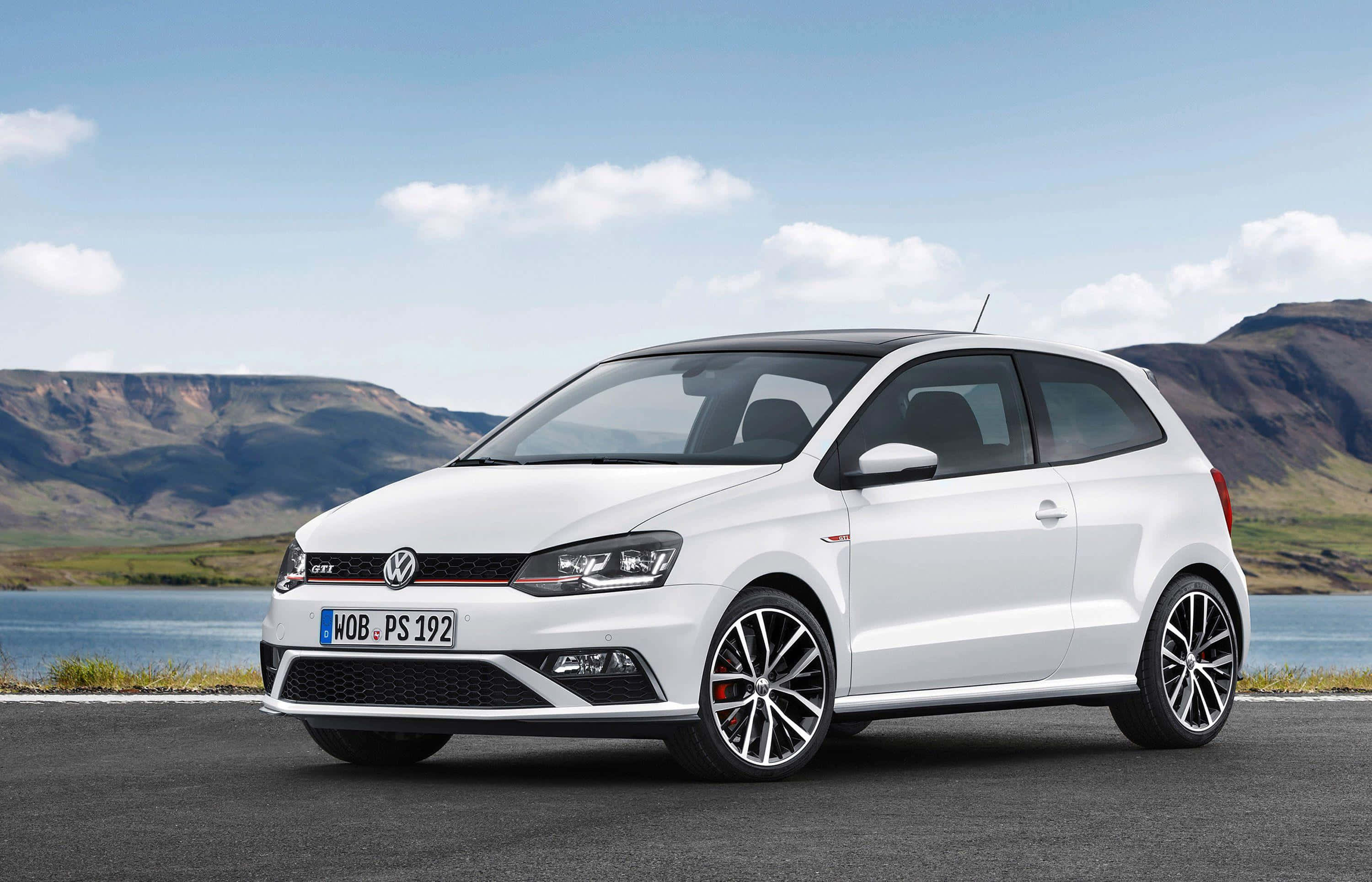 Volkswagen Polo 桌布 壁紙 — 一架時尚的白色福士Polo GTI停泊在湖邊的道路上，背景是起伏的丘陵，天空部分多雲。