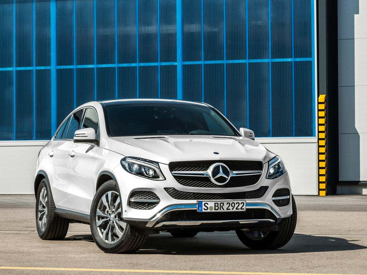 Mercedes Benz Gle-class 桌布 壁紙 — 一架時尚的白色 Mercedes GLE Coupe 停泊在現代藍色玻璃建築前，沐浴在明亮的日光下。