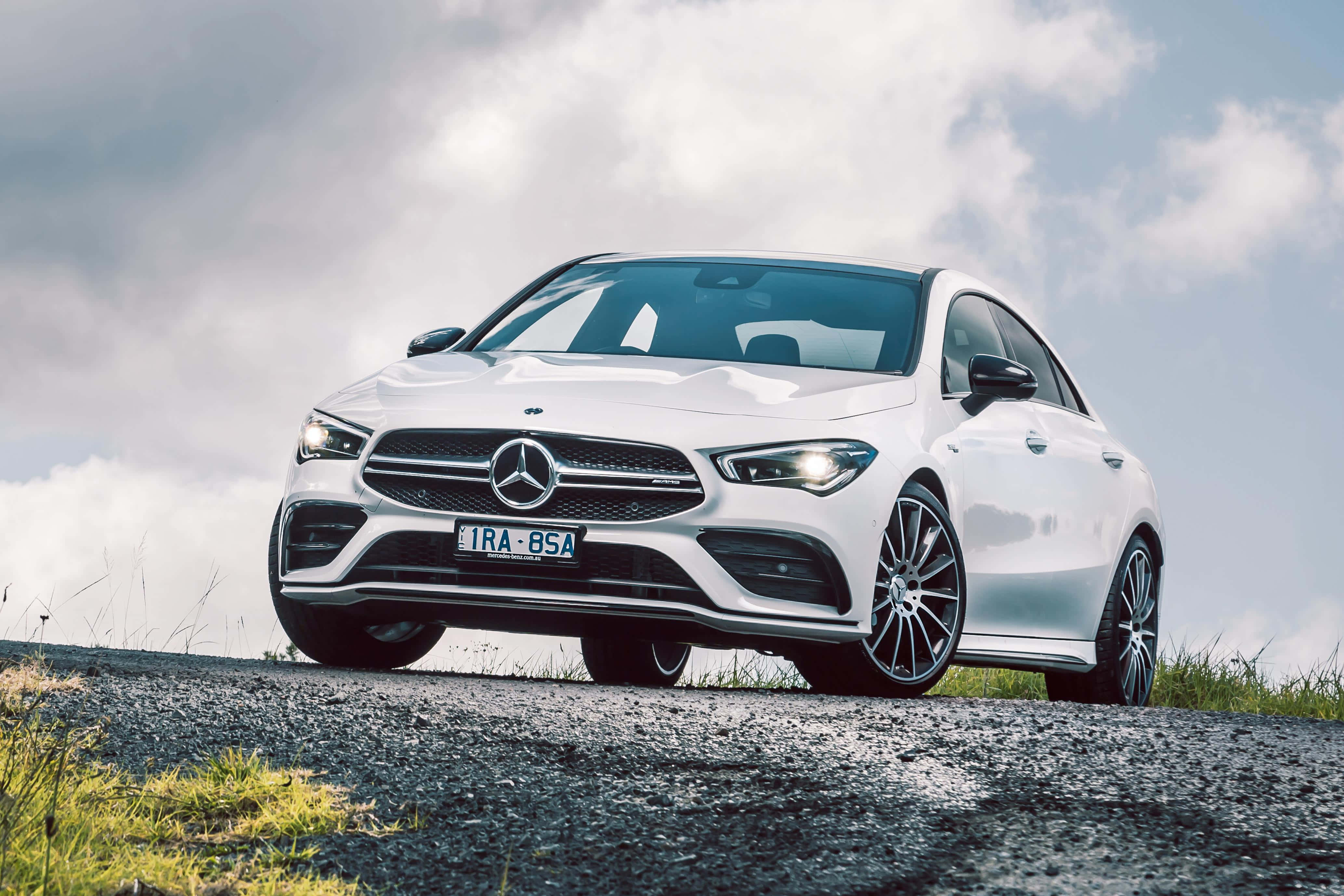 Mercedes Benz Cla-class 桌布 壁紙 — 一架時尚的白色平治CLA轎跑車停泊在碎石路上，天空多雲，路邊有草叢。