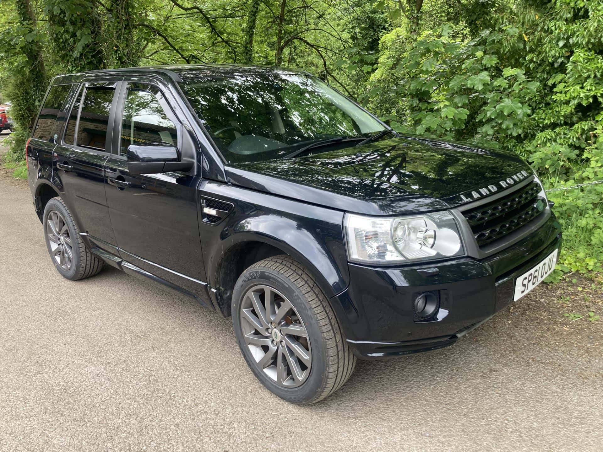 Land Rover Freelander 桌布 壁紙 — 一架時尚的黑色 Land Rover Freelander 停泊在碎石路上，周圍是茂密的綠色樹葉。